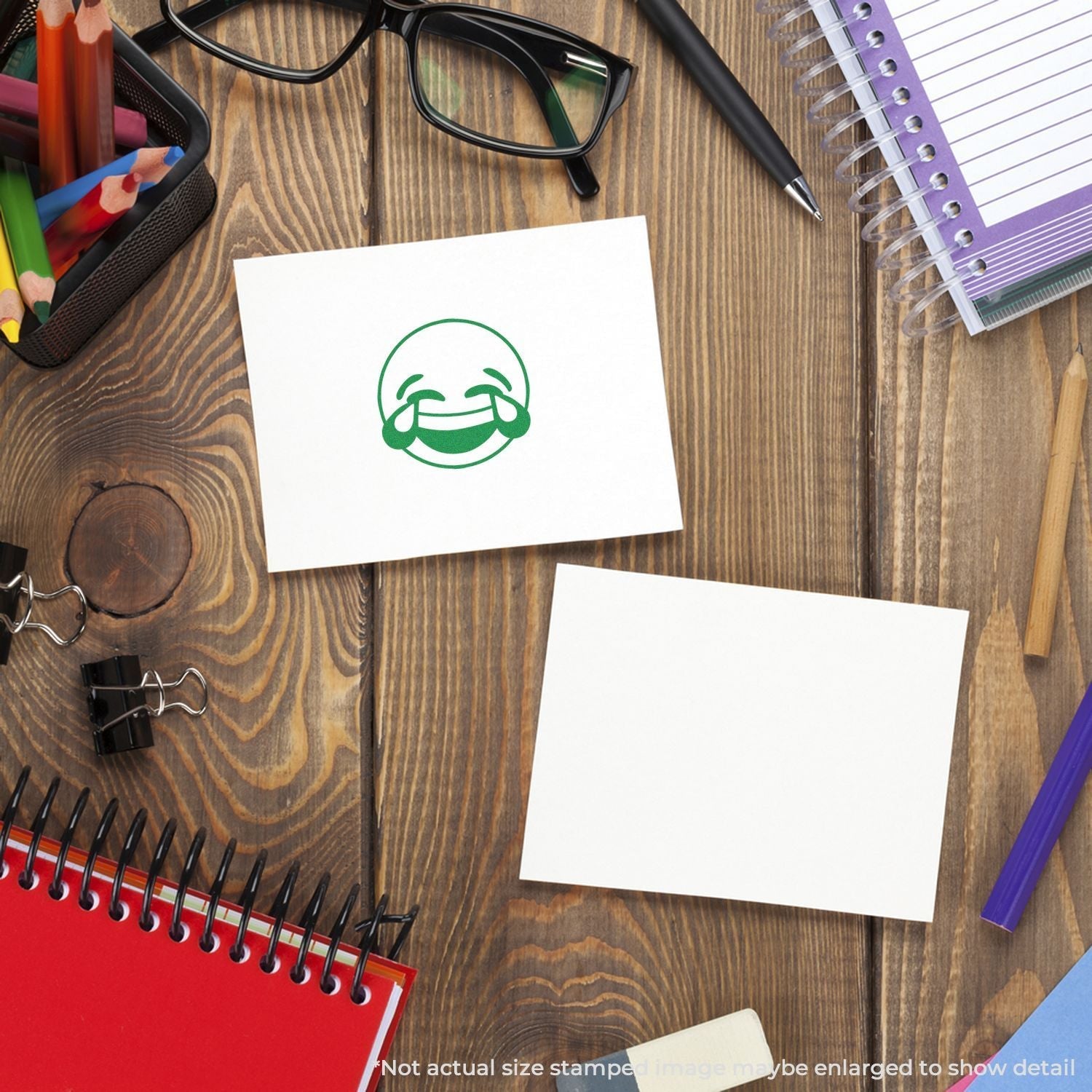 Self Inking Round Laughing Smiley Stamp on a wooden desk with stationery items, showing a green laughing smiley face on a white card.