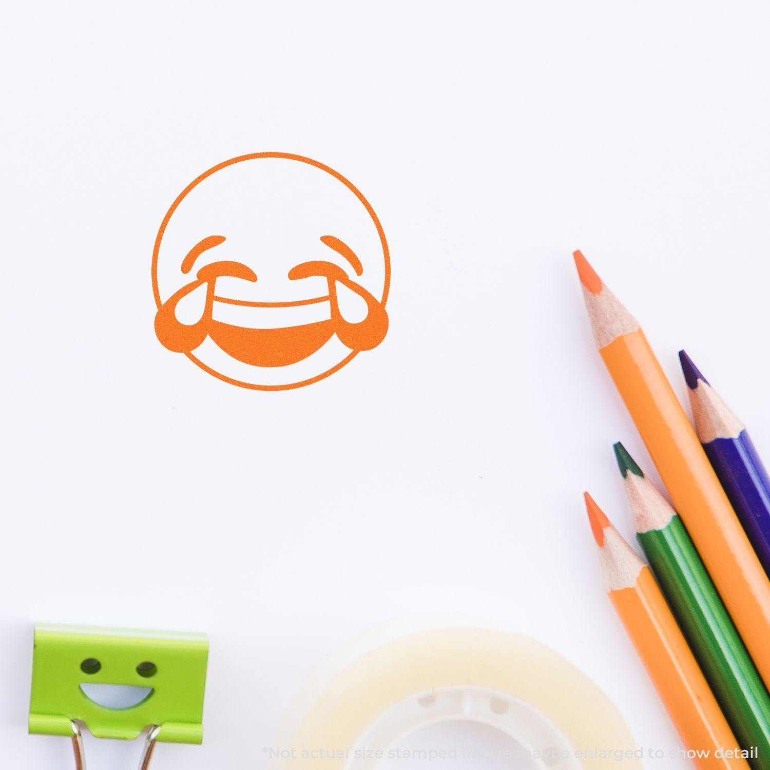 Round Laughing Smiley Rubber Stamp impression on white paper, surrounded by colored pencils, a smiley clip, and tape.