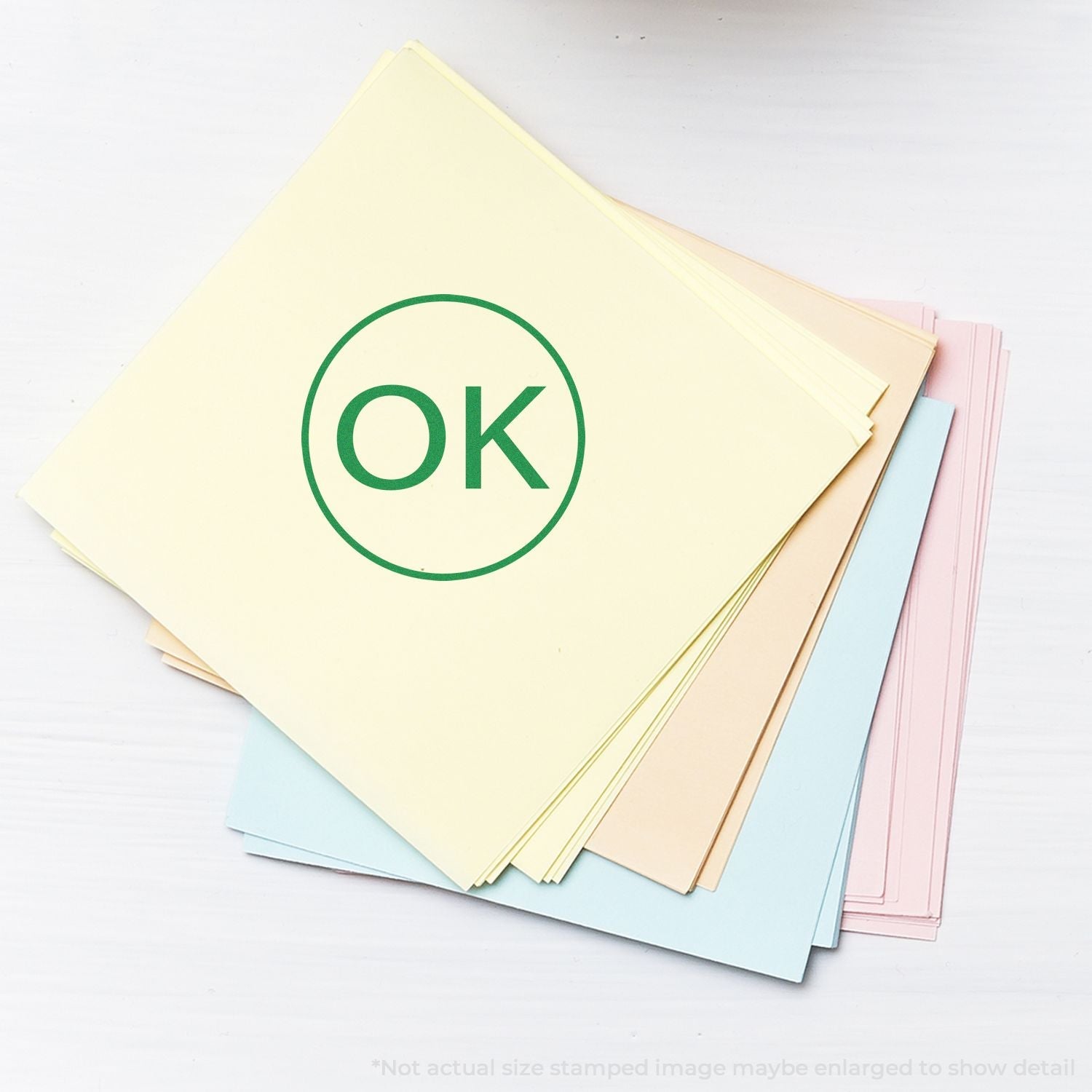 Self Inking Round OK Stamp imprint in green on a stack of pastel-colored papers, showcasing the stamp's clear and bold marking.