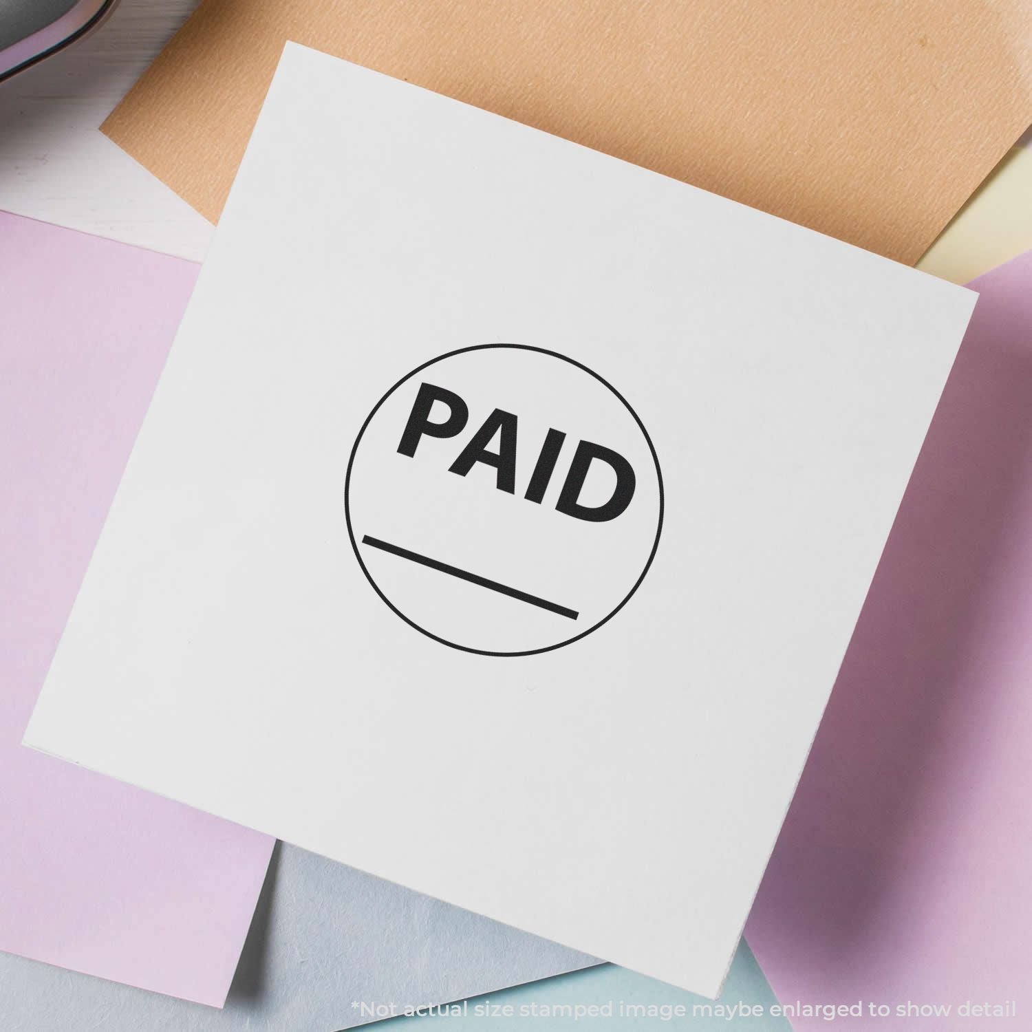 Self Inking Round Paid with Line Stamp on white paper, surrounded by pastel-colored sheets.