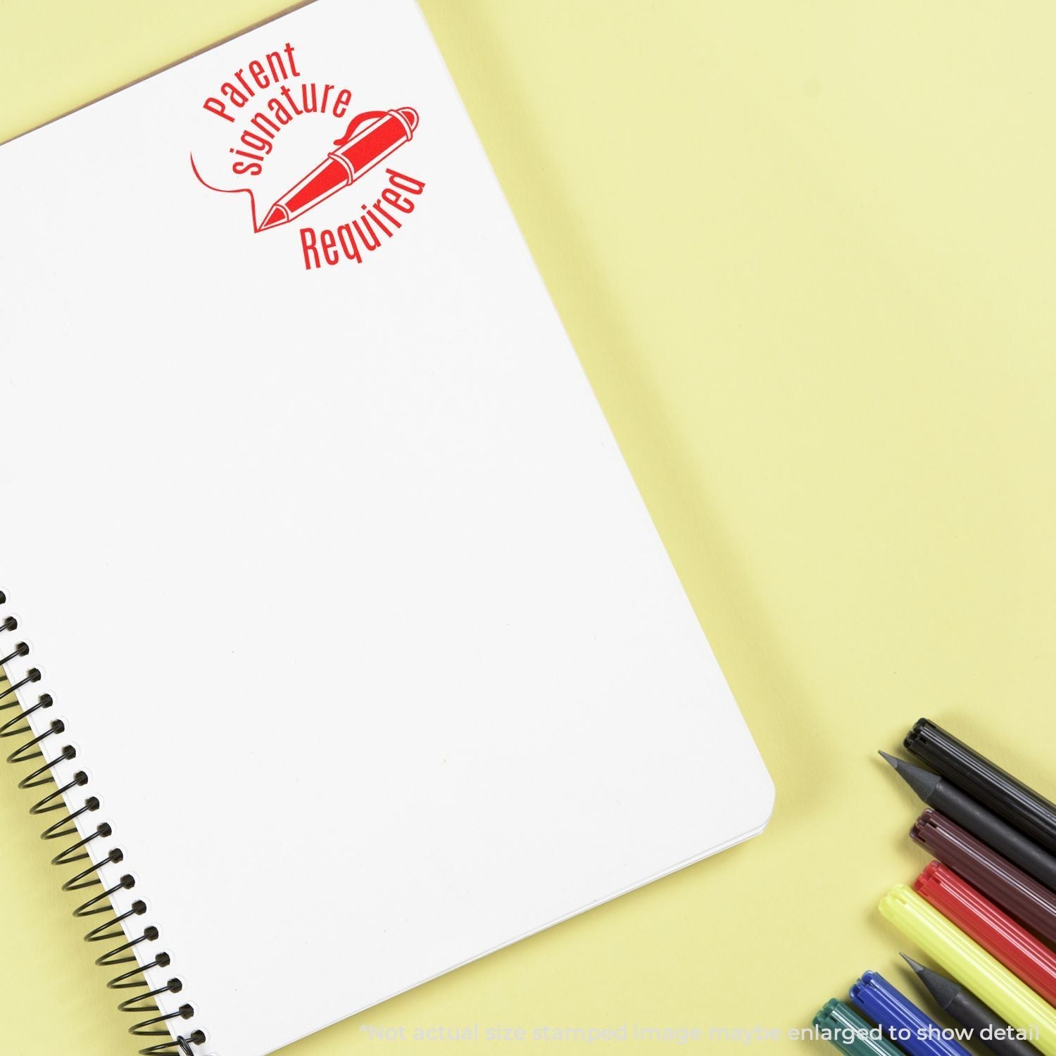 Self Inking Round Parent Signature Required Stamp in red ink on a white spiral notebook, with colored pens on a yellow background.