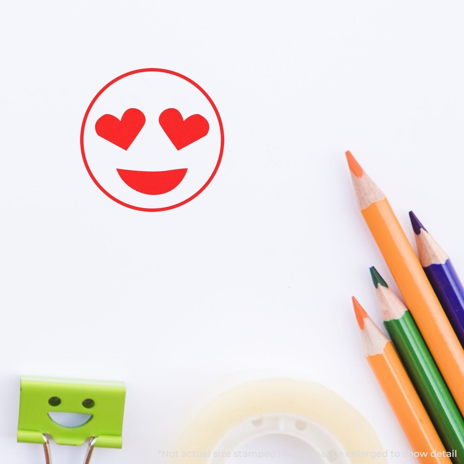 Self Inking Round Smiley with Hearts Stamp in red ink on white paper, surrounded by colorful pencils, a green clip, and tape.