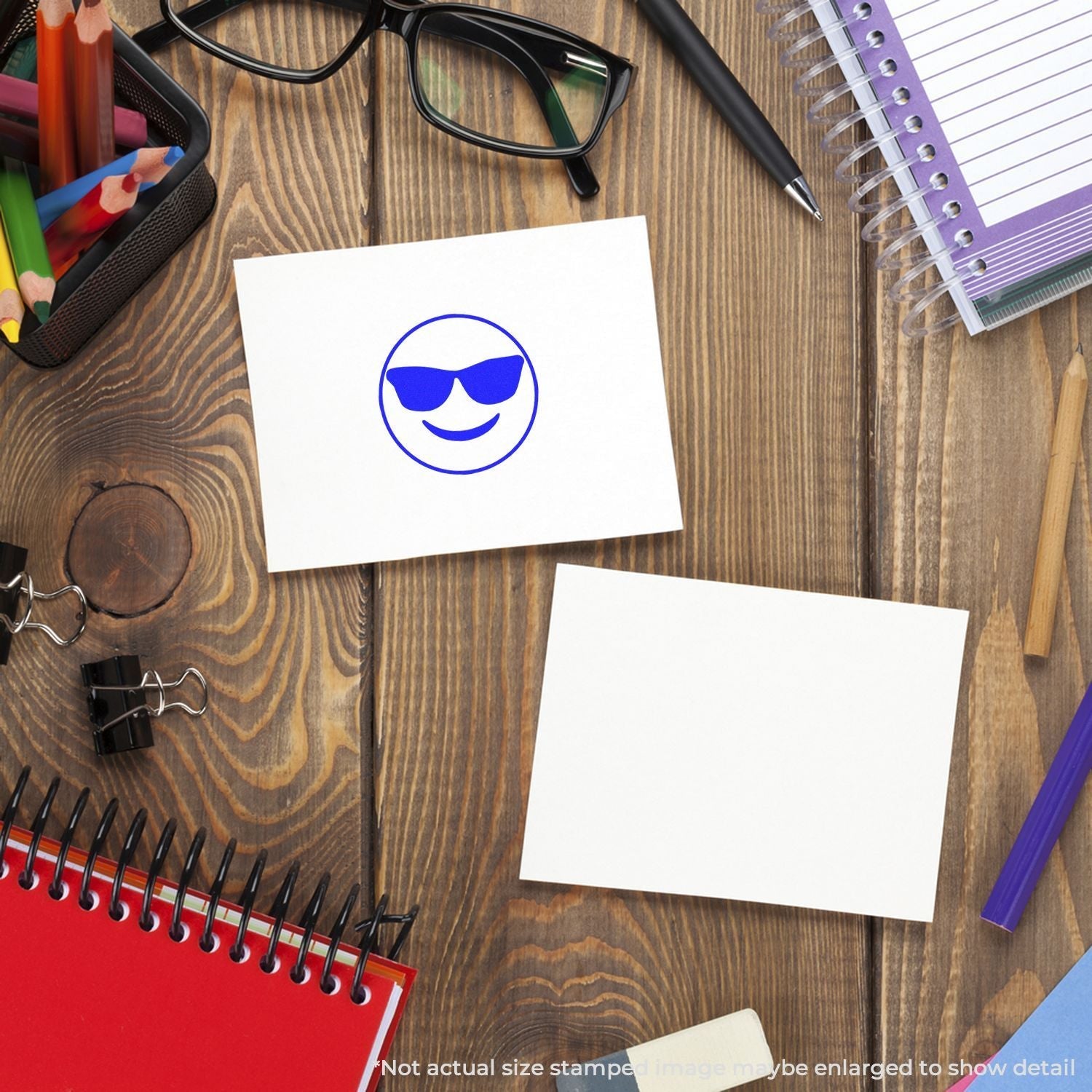 Self Inking Round Smiley with Sunglasses Stamp on a white card, surrounded by office supplies on a wooden desk.