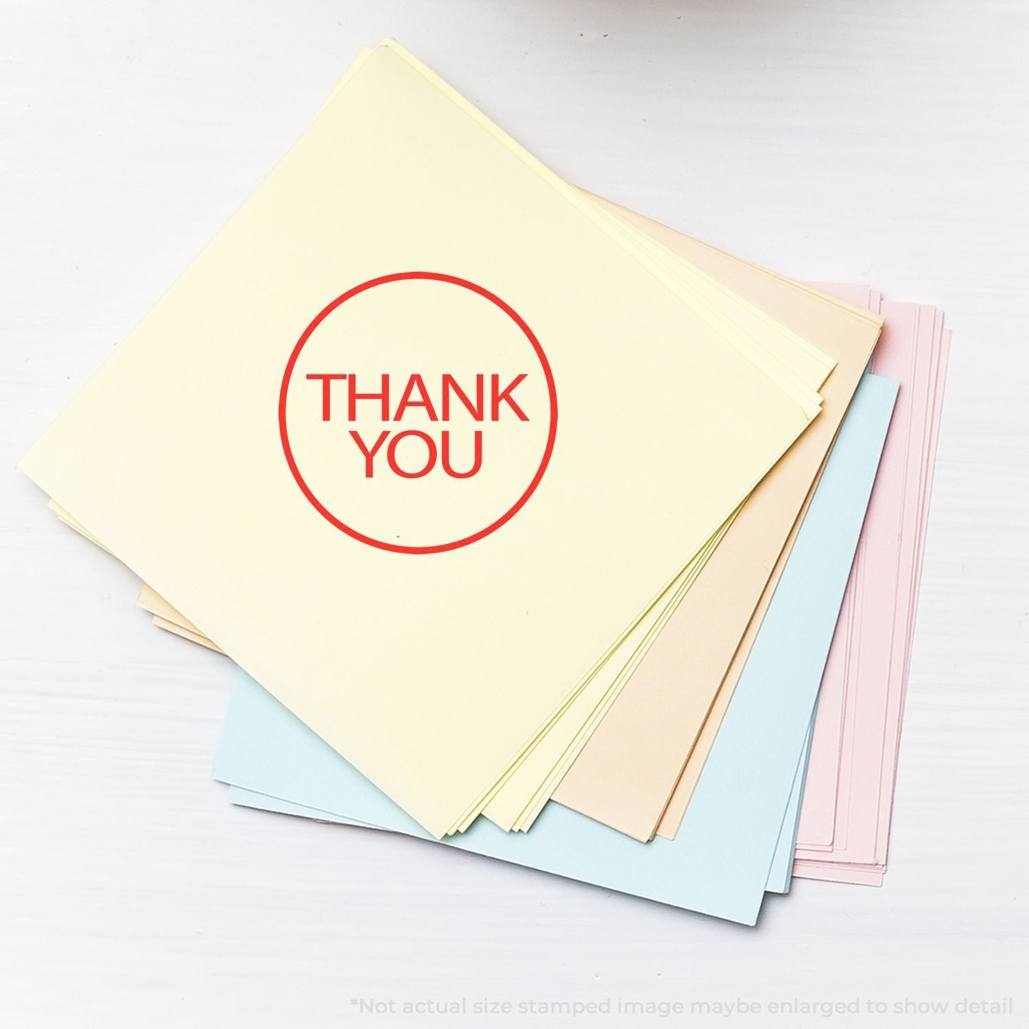 Self Inking Round Thank You Stamp on a stack of pastel-colored papers, displaying a clear red THANK YOU message in a circular design.