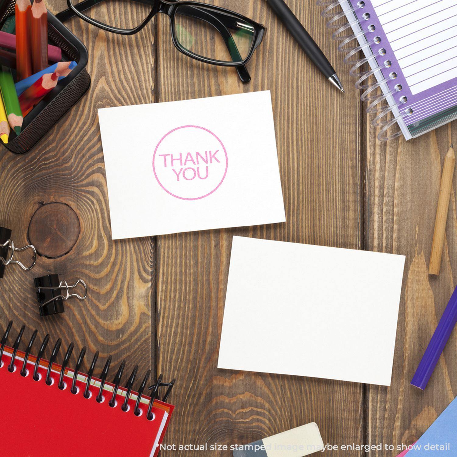 Round Thank You Rubber Stamp on a white card, surrounded by office supplies like notebooks, glasses, and pens on a wooden desk.