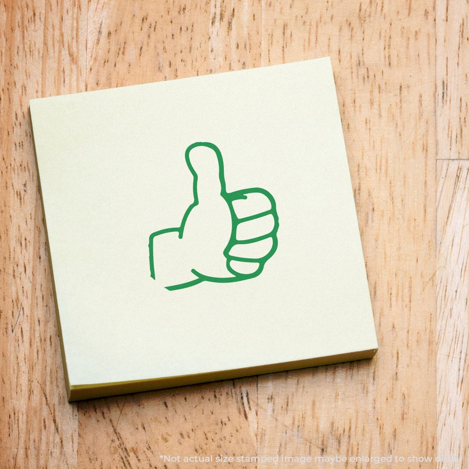 Self Inking Round Thumbs Up Stamp used on a yellow sticky note, displaying a green thumbs-up symbol on a wooden surface.