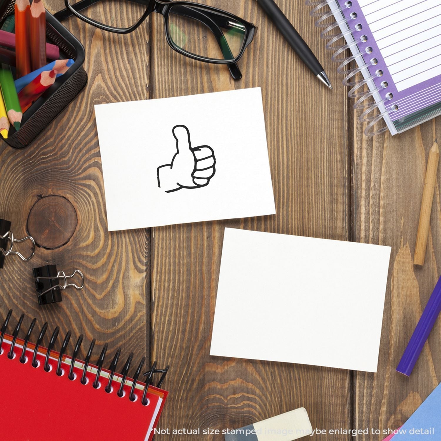 Self Inking Round Thumbs Up Stamp on a wooden desk with stationery items, showing a thumbs-up mark on a white card.