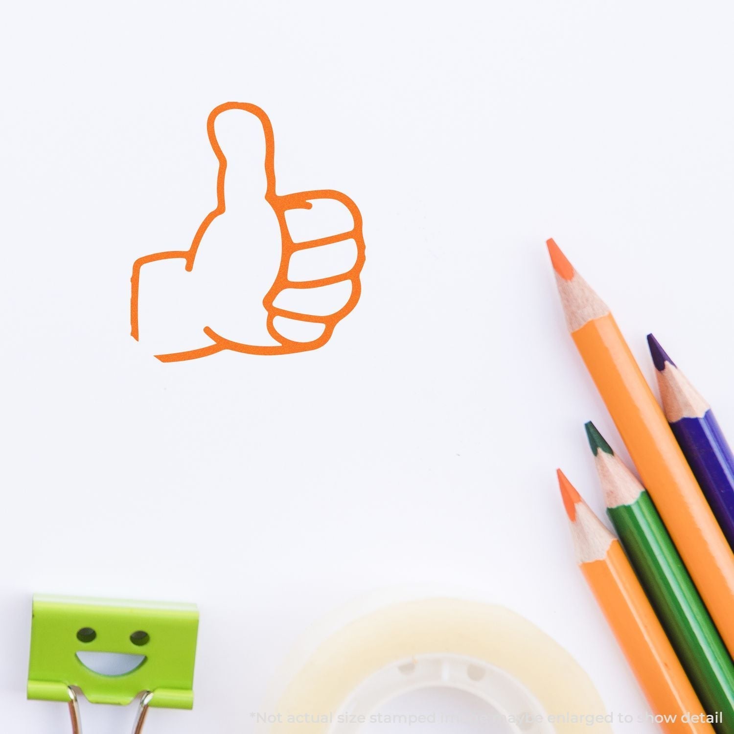 Self Inking Round Thumbs Up Stamp in use, showing an orange thumbs-up mark on paper, with colored pencils, tape, and a smiling clip nearby.