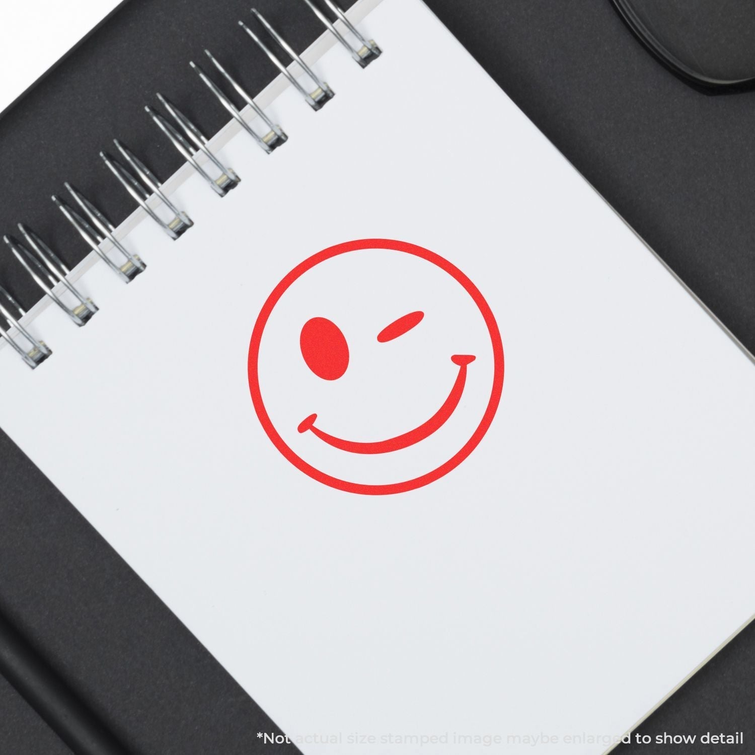 Self Inking Round Winking Smiley Stamp in red ink on a white spiral notebook, creating a playful and cheerful impression.