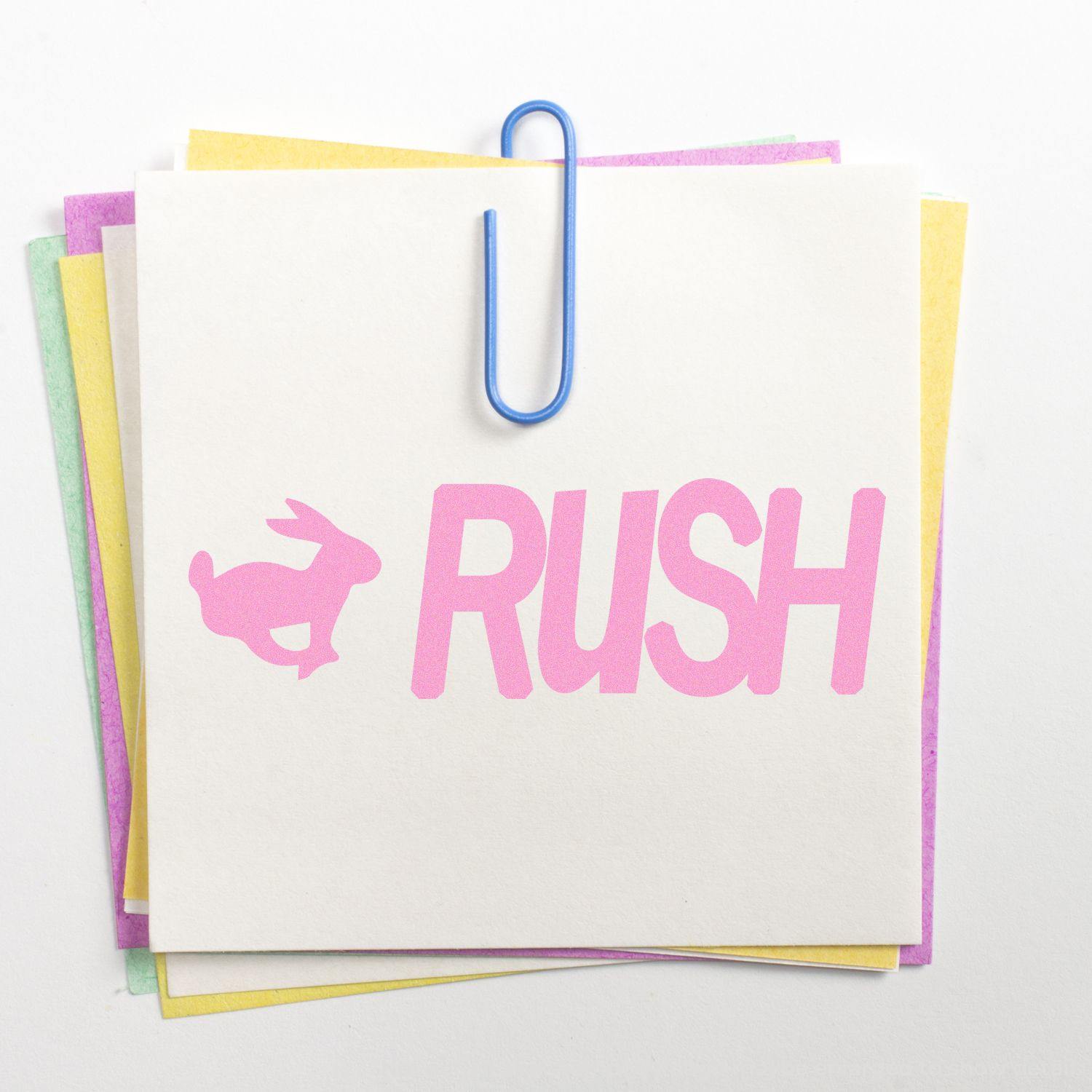 Large Pre-Inked Rush with Rabbit Stamp in pink ink on a white note, clipped with a blue paperclip to colorful papers.