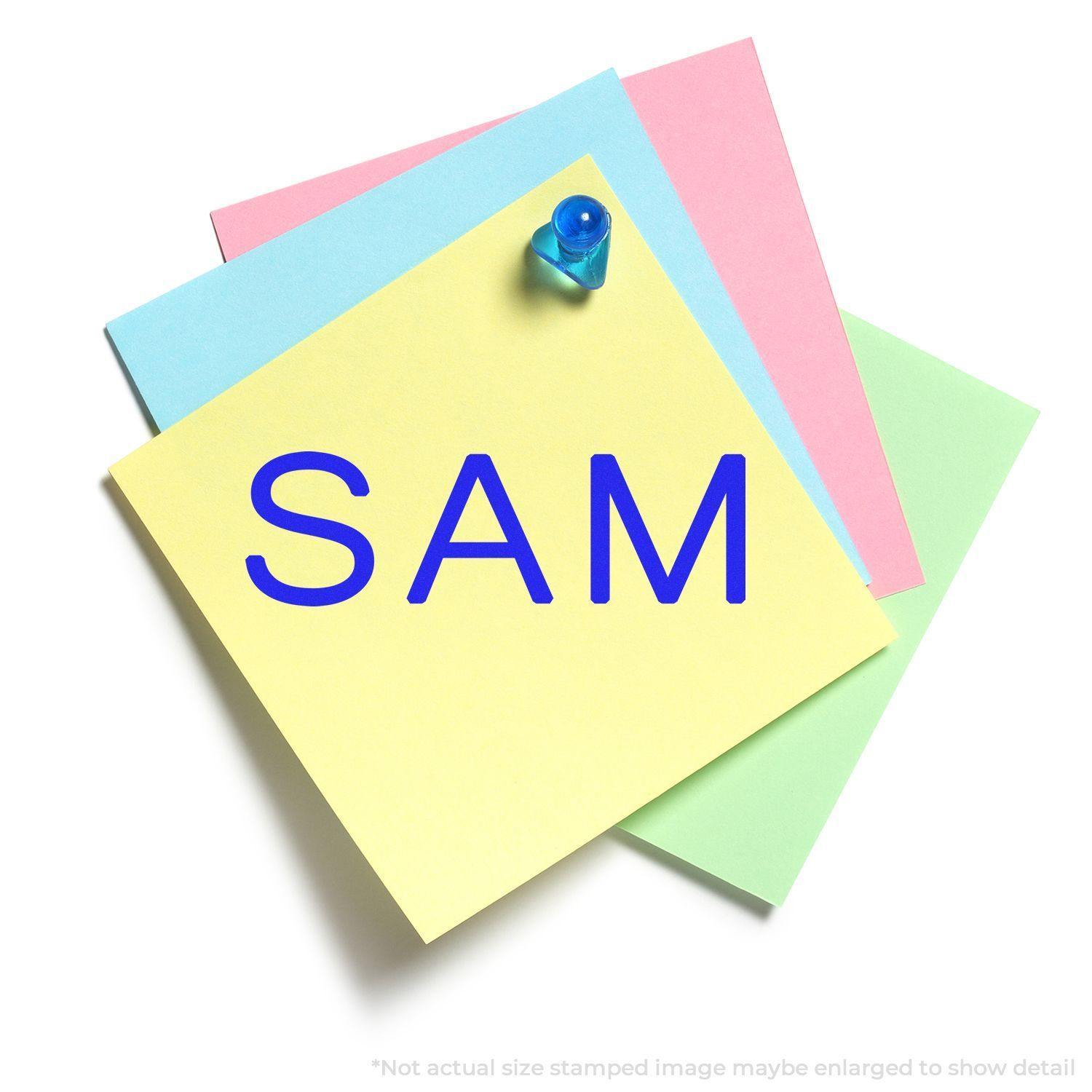 Large Pre-Inked SAM Stamp imprint on a yellow sticky note pinned to a stack of colorful sticky notes.