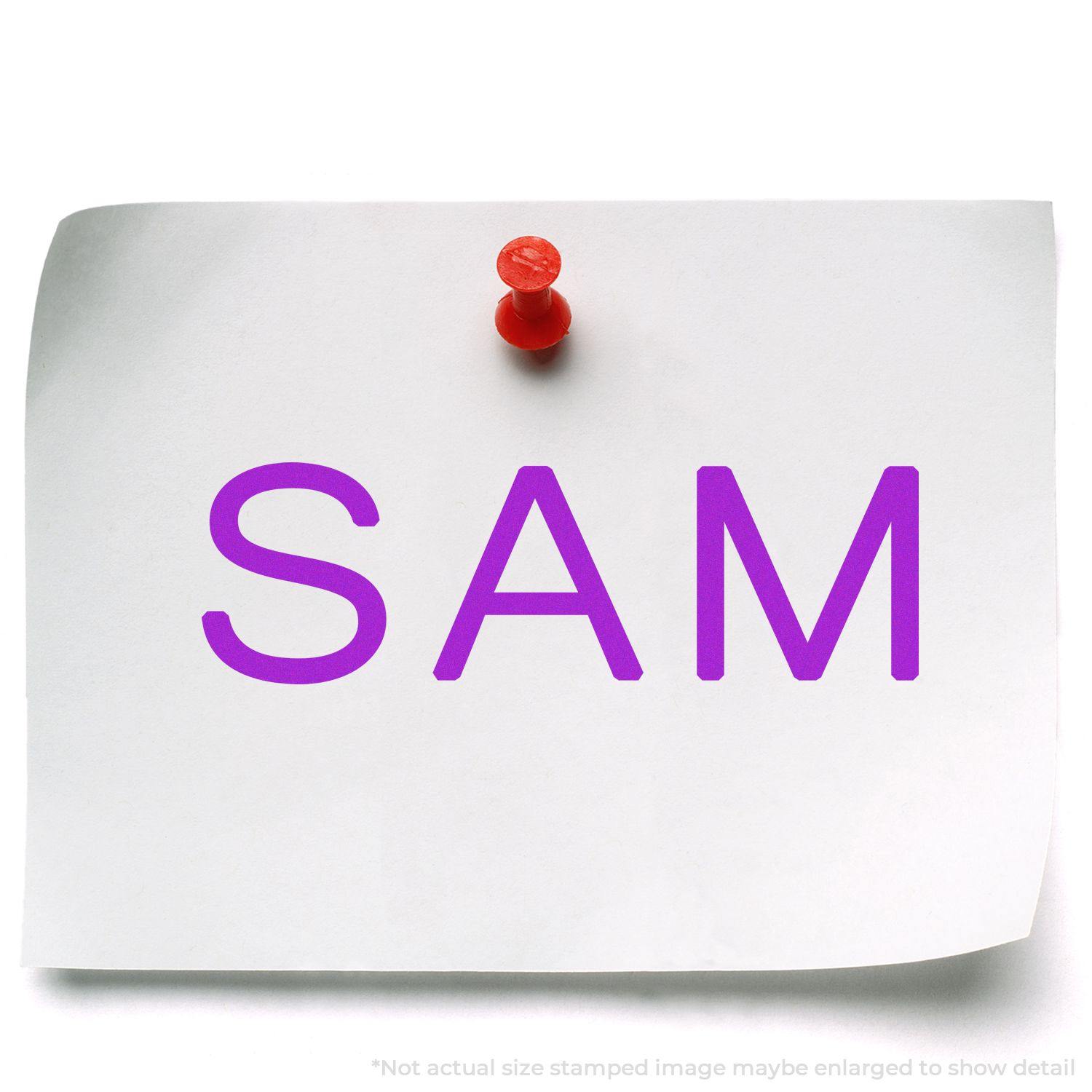 A piece of white paper pinned to a board with a red pushpin, stamped with SAM in purple using the Large Pre-Inked SAM Stamp.