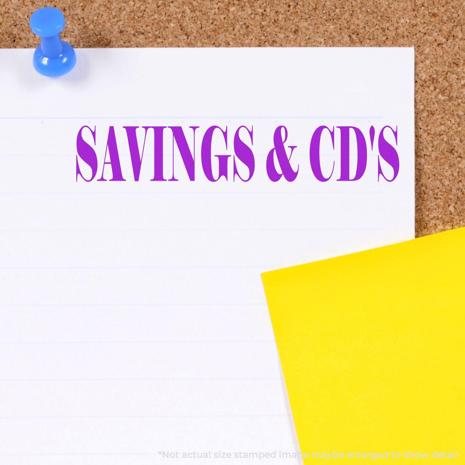 Large Pre-Inked Savings & CD's Stamp in purple ink on a white paper pinned to a corkboard, with a yellow sticky note nearby.