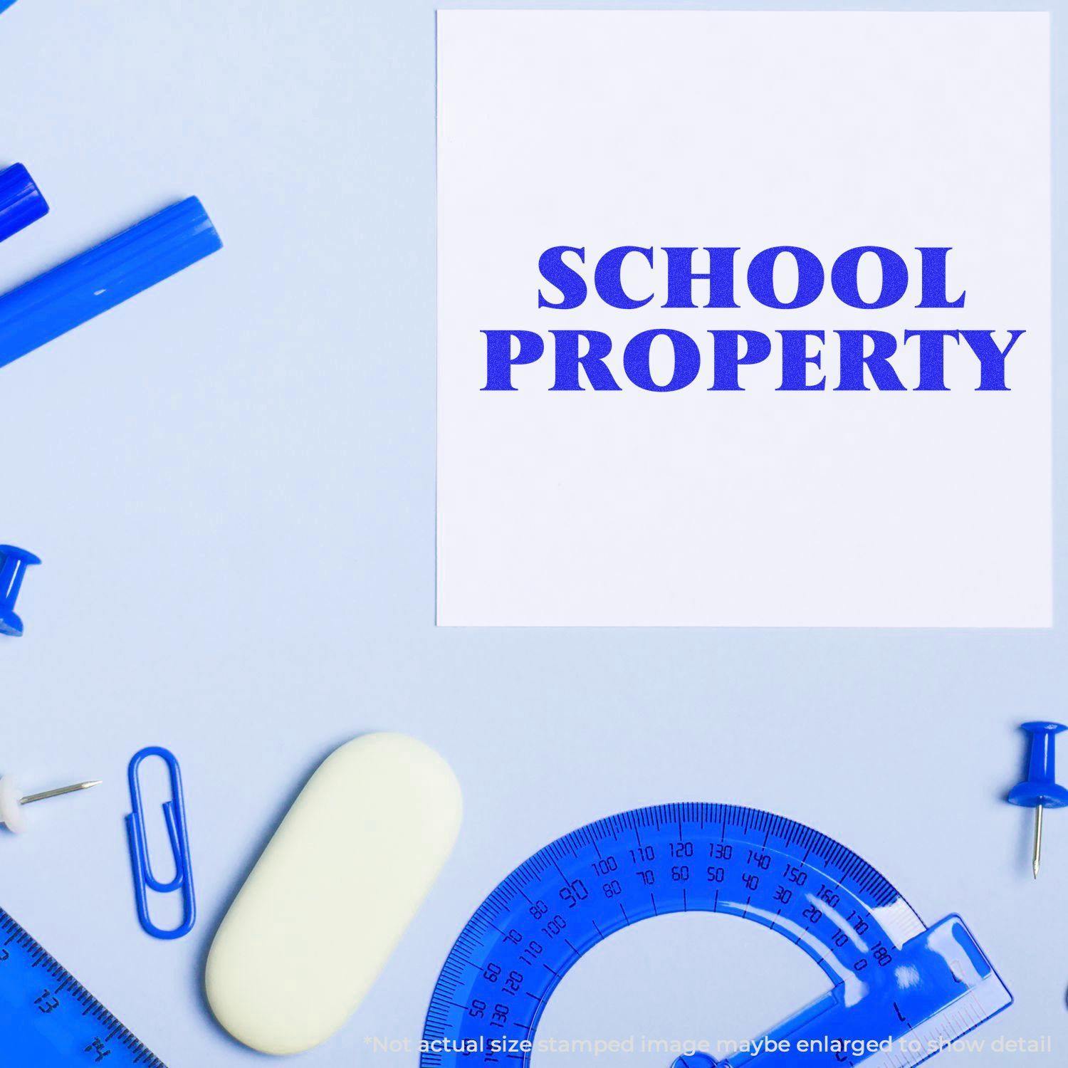 Slim Pre-Inked School Property Stamp used on paper, surrounded by blue stationery items like rulers, pens, and paper clips.