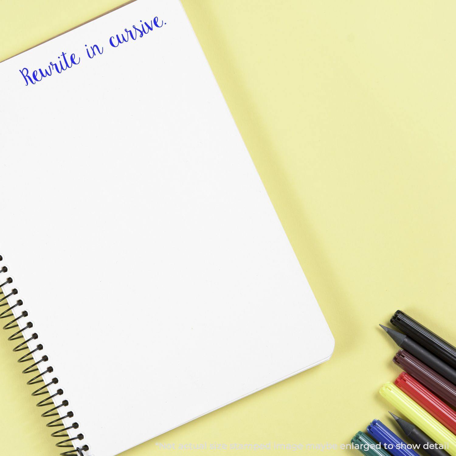 Spiral notebook with Rewrite in cursive stamped in blue ink, surrounded by colorful pens on a yellow background.