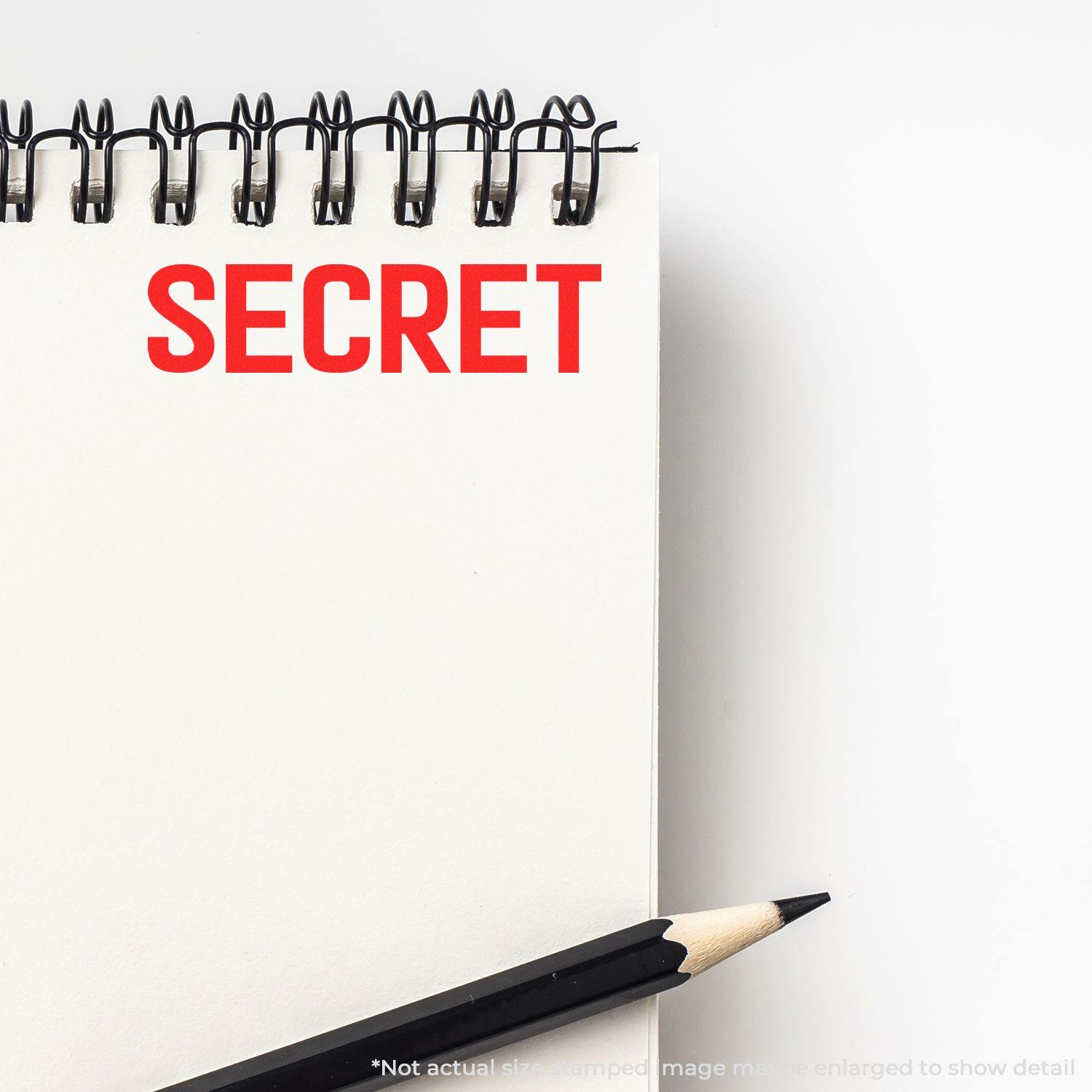 A notebook with the word SECRET stamped in red using the Large Secret Rubber Stamp, with a pencil placed beside it.