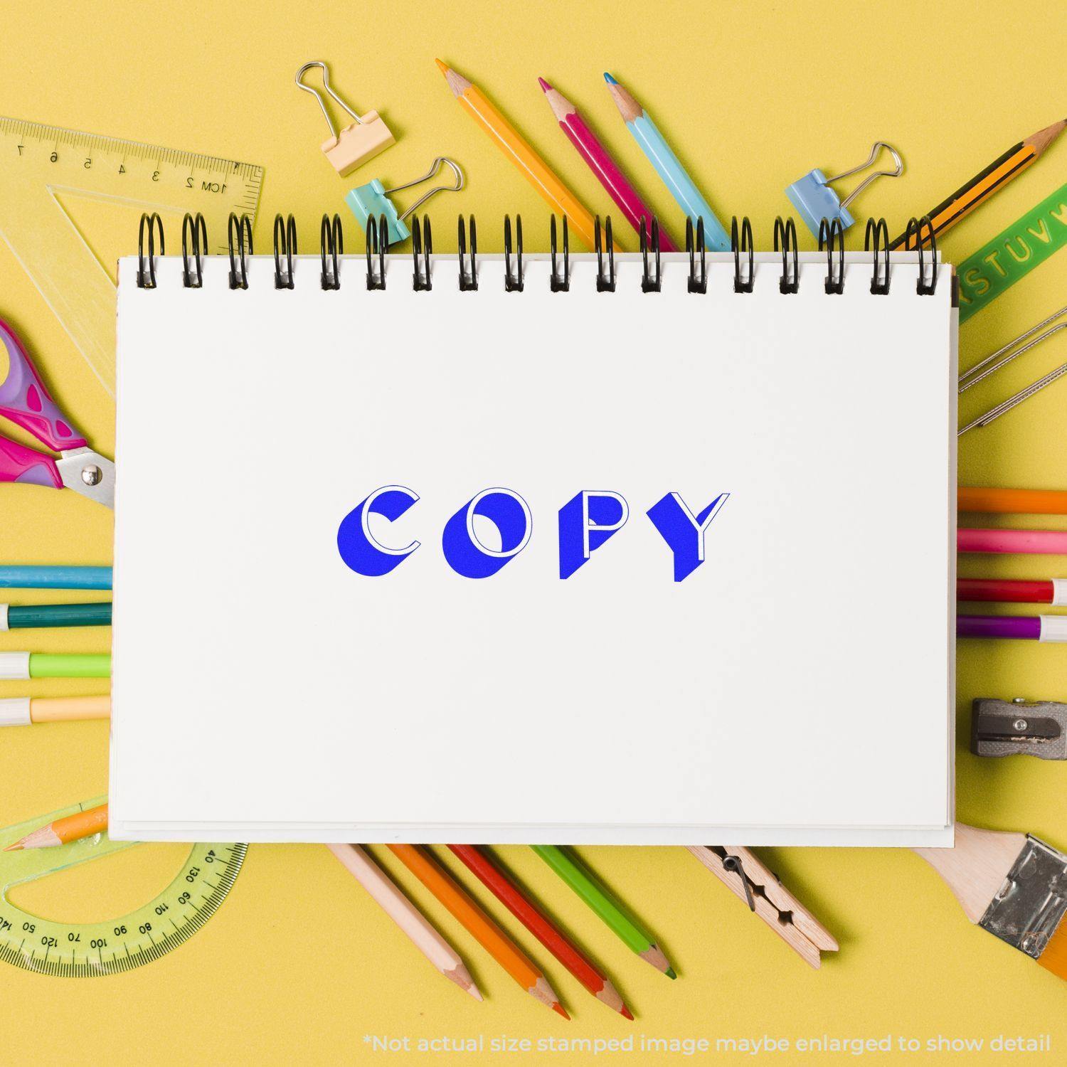 A notebook stamped with COPY using the Large Pre-Inked Shadow Copy Stamp, surrounded by colorful stationery on a yellow background.