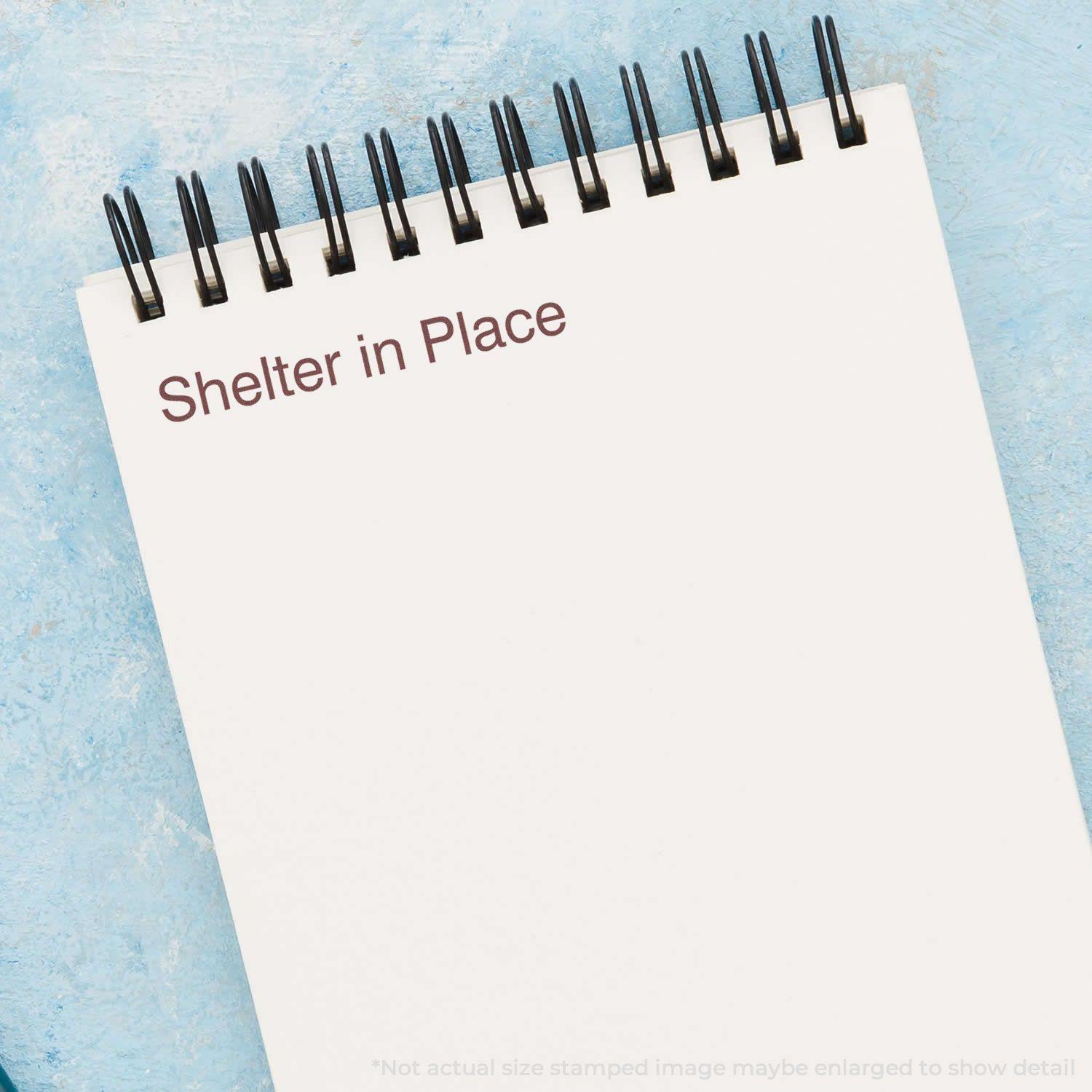 Self Inking Shelter in Place Stamp used on a spiral notebook, displaying the text Shelter in Place on a light blue background.