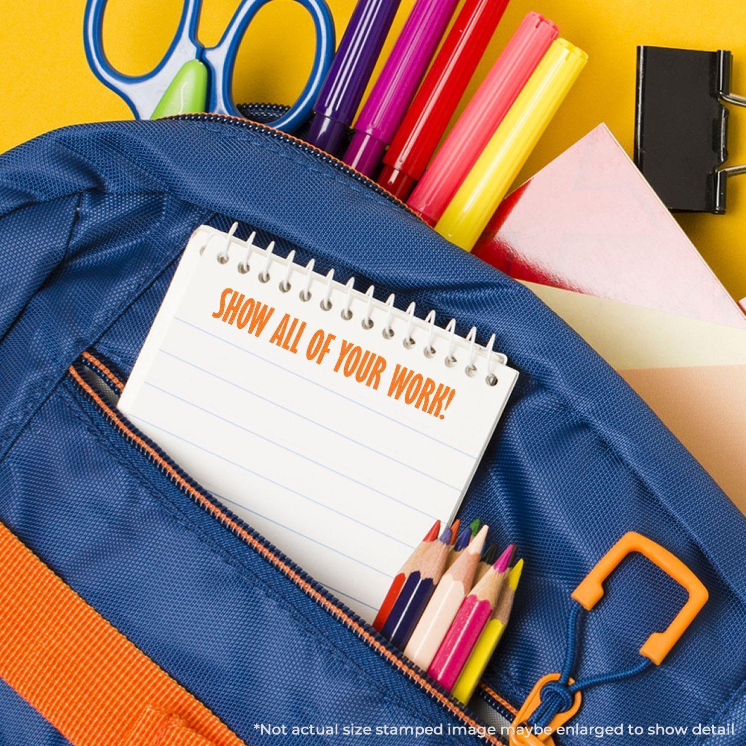 A Large Self Inking Show All Of Your Work Stamp is used on a notebook, surrounded by school supplies like pencils, scissors, and markers.