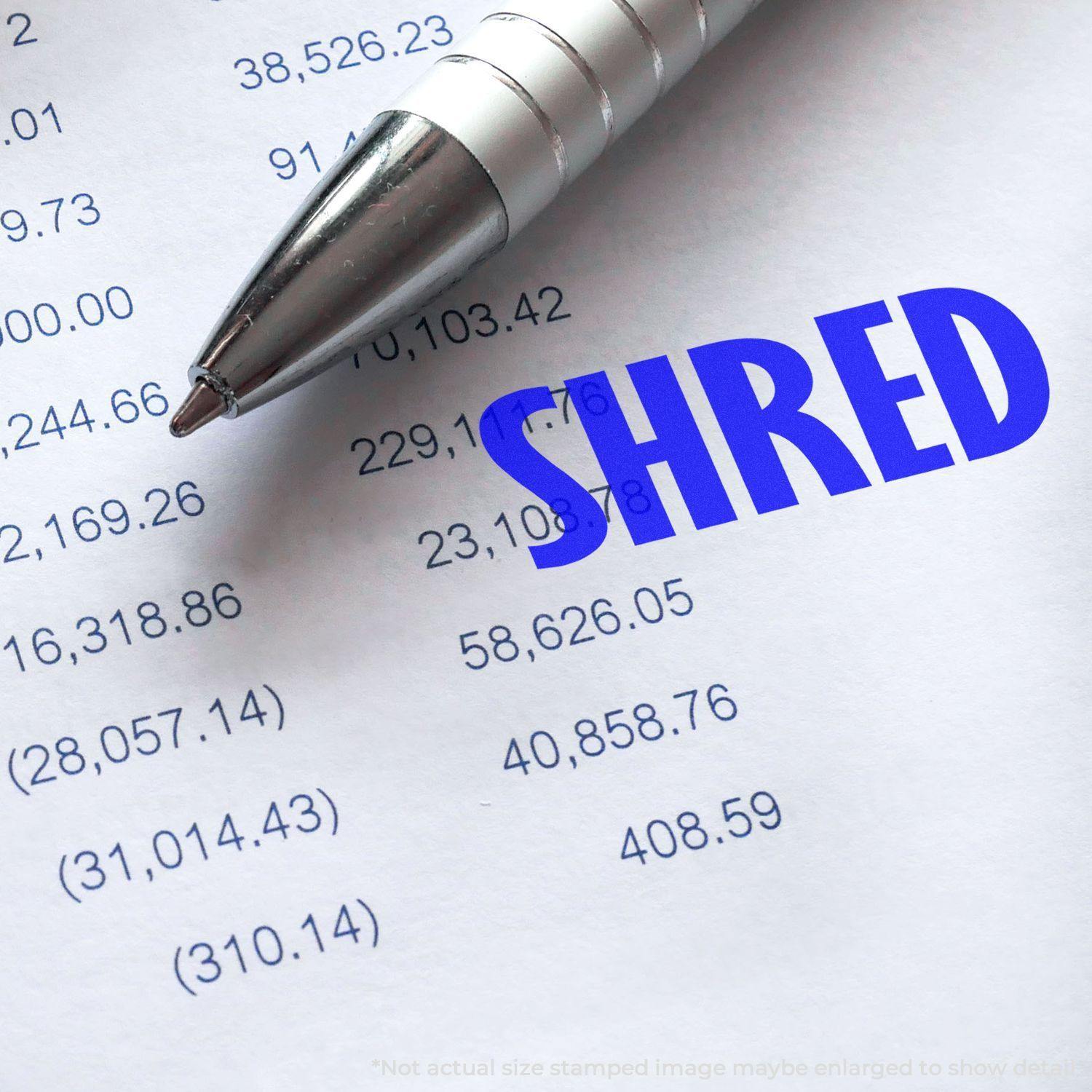 A pen next to a document stamped with SHRED using the Large Pre-Inked Shred Stamp, obscuring sensitive information on the paper.