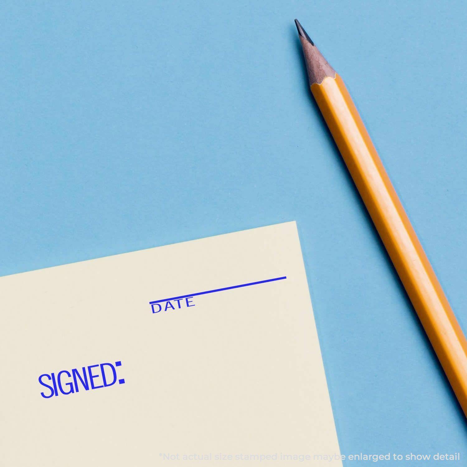 Large Self Inking Signed with Date Stamp used on paper, next to a yellow pencil on a blue background.