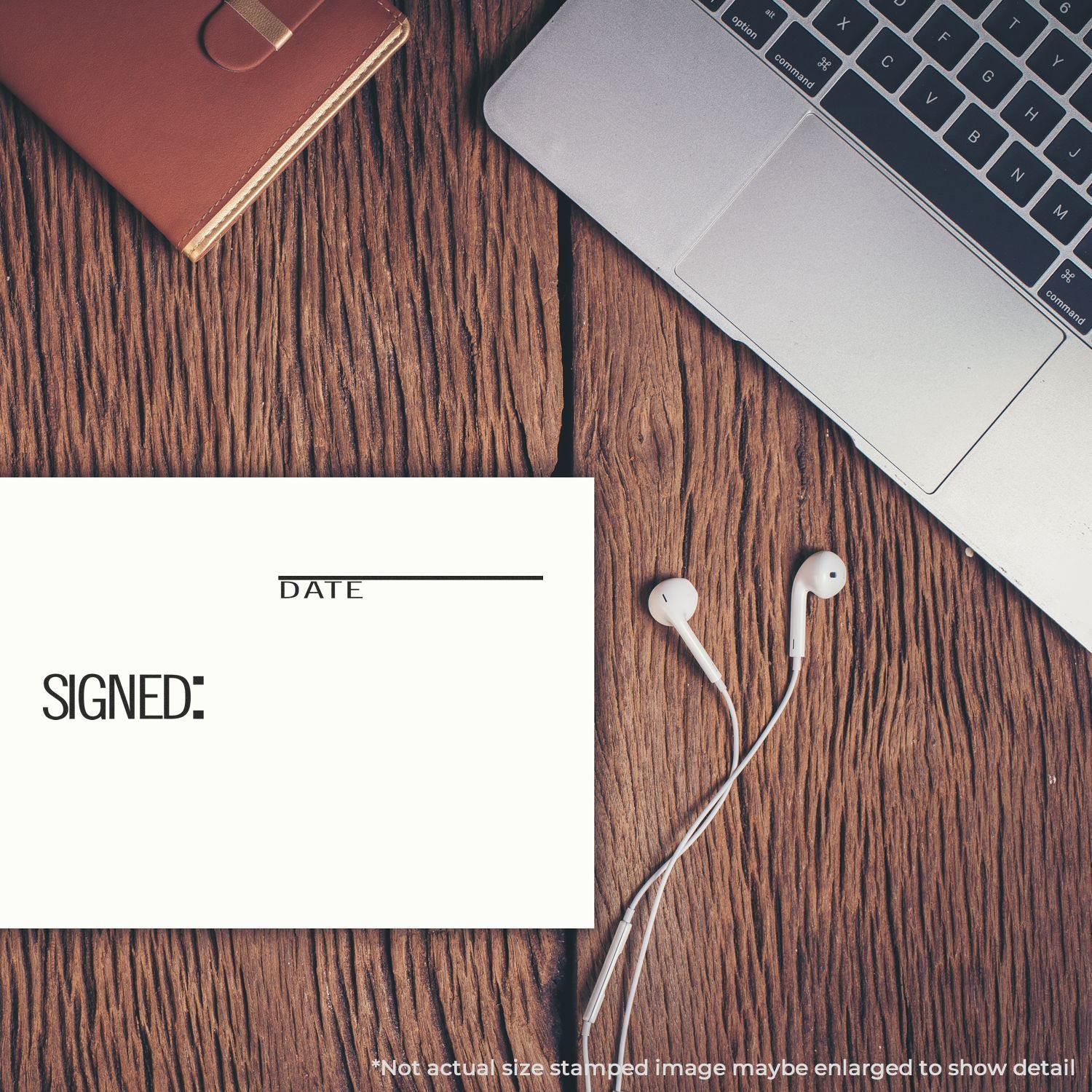 Large Self Inking Signed with Date Stamp on paper beside a laptop, notebook, and earphones on a wooden desk.