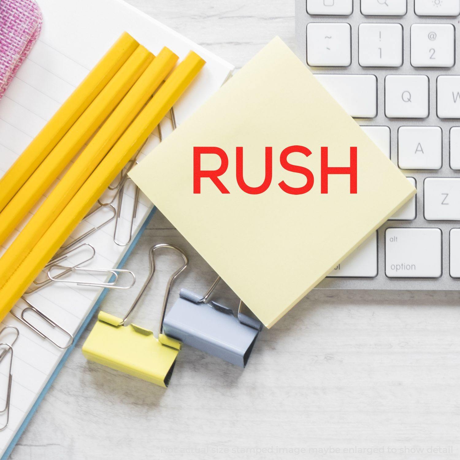 Self Inking Skinny Rush Stamp marking RUSH on a sticky note, surrounded by office supplies and a keyboard.