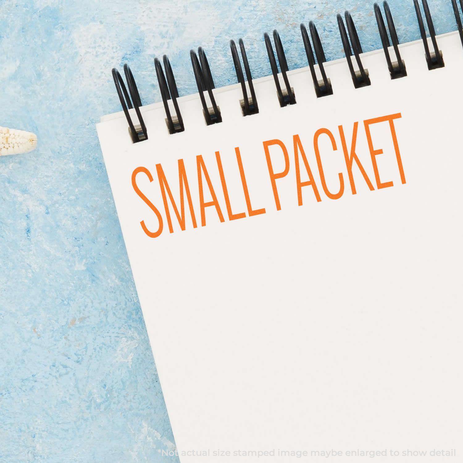 Self Inking Small Packet Stamp used on a white spiral notebook, displaying the text SMALL PACKET in orange on a light blue background.