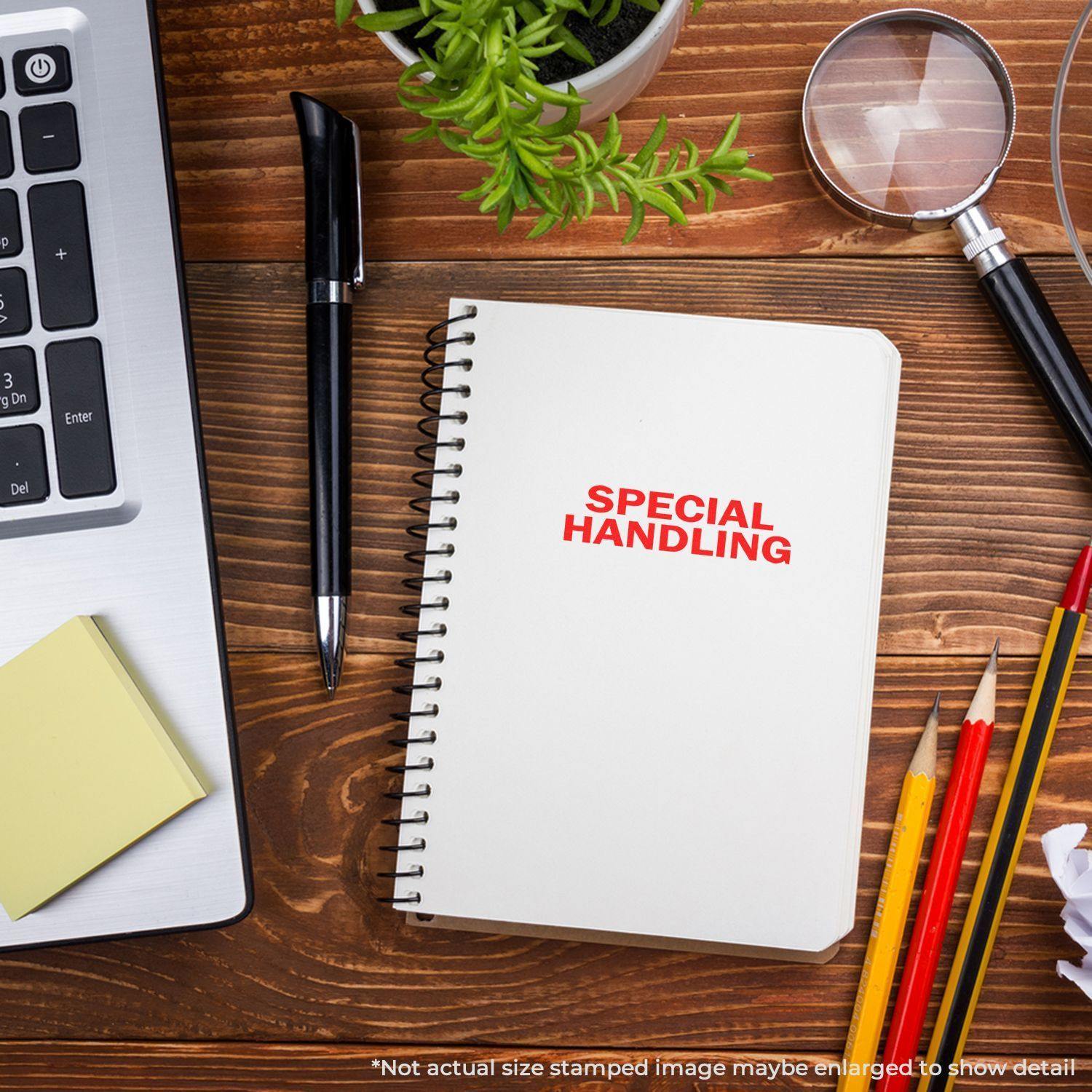 Self Inking Special Handling Stamp on a notebook, surrounded by a laptop, pen, magnifying glass, plant, and colored pencils on a wooden desk.