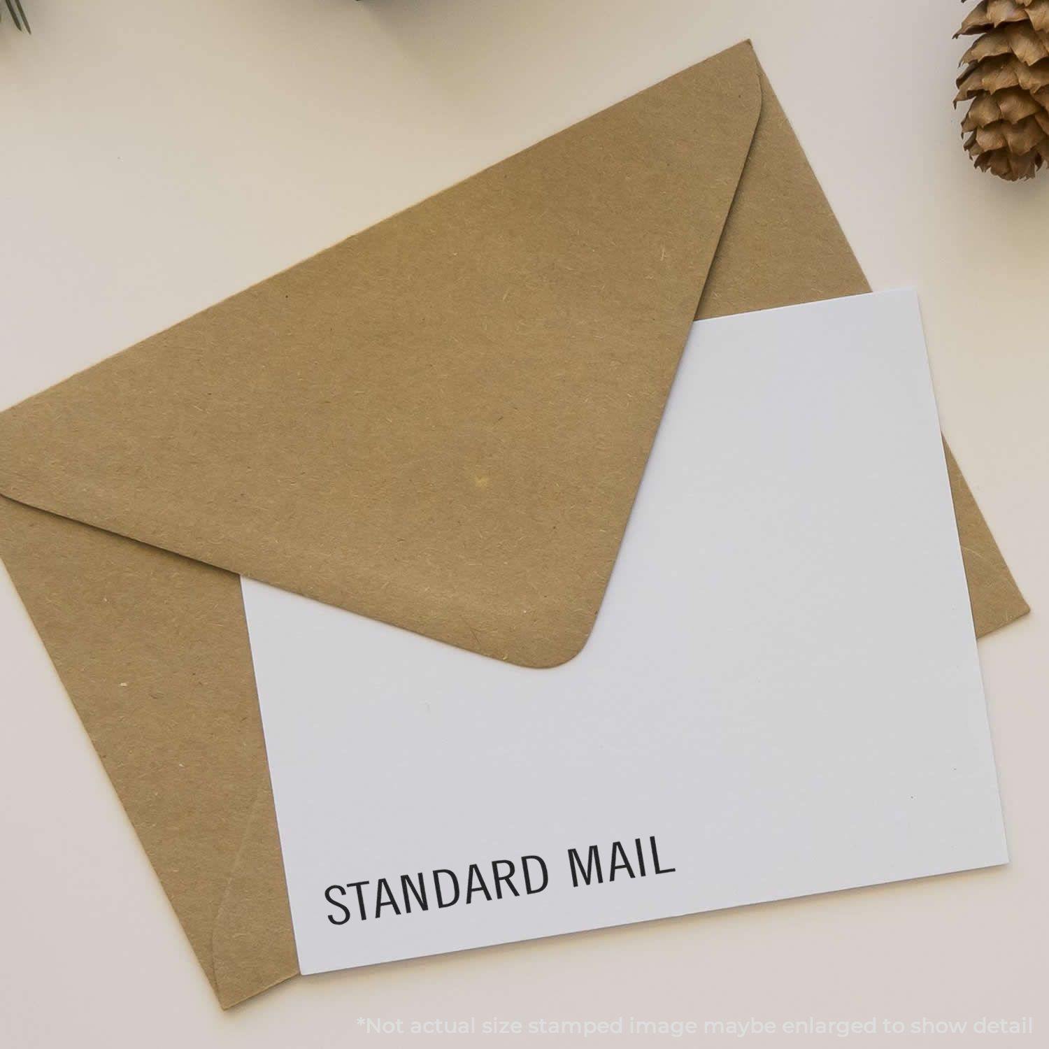 Brown envelope with a white card stamped Standard Mail Rubber Stamp in black ink, placed on a light-colored surface.