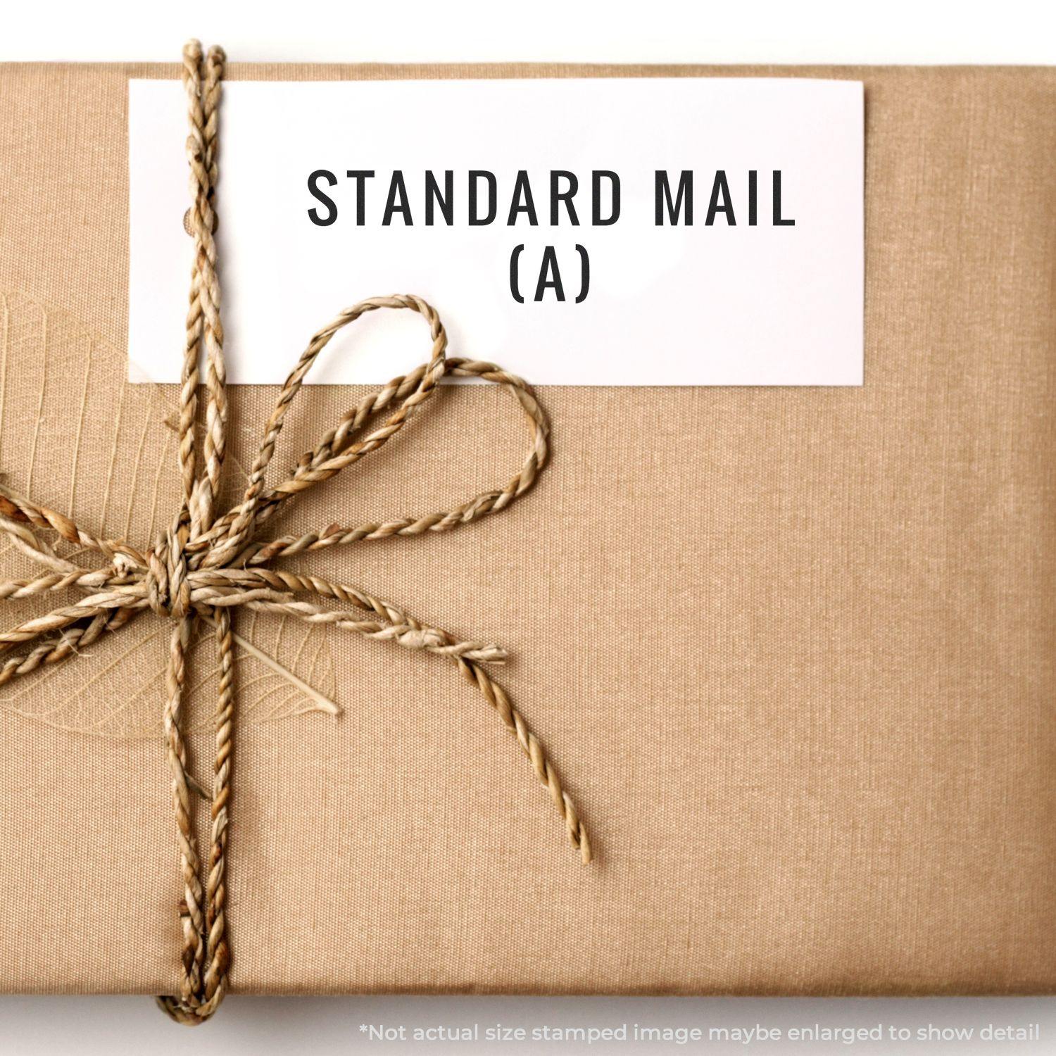 A brown package with a twine bow and a white label stamped with STANDARD MAIL (A) using the Self Inking Standard Mail (A) Stamp.