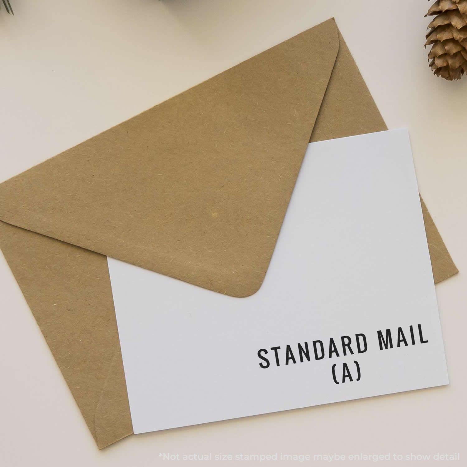 Envelope with a card stamped Standard Mail (A) in black ink, placed on a beige surface with a pinecone in the corner.