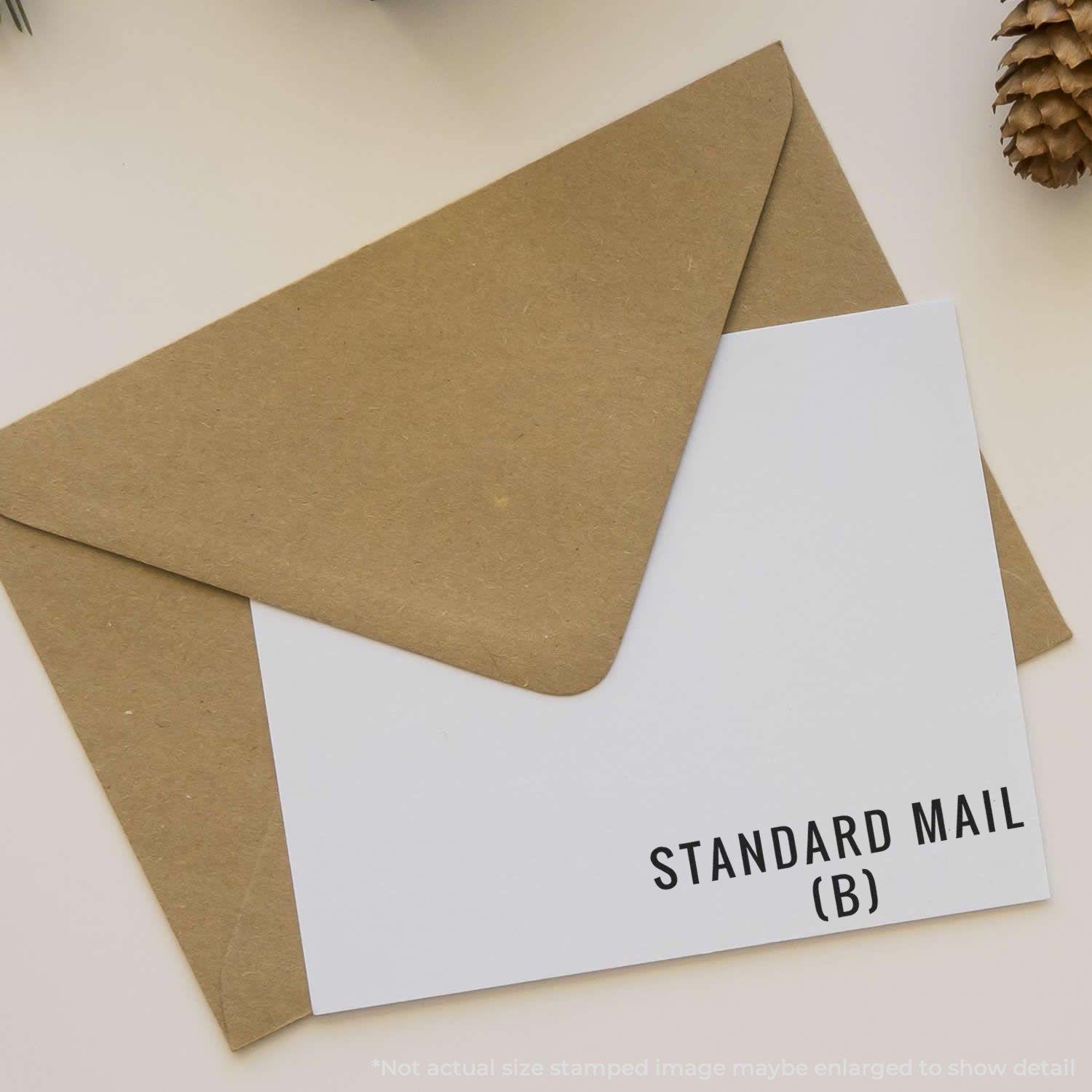 Large Pre-Inked Standard Mail (B) Stamp used on a white card placed inside a brown envelope, with pinecone decoration in the background.