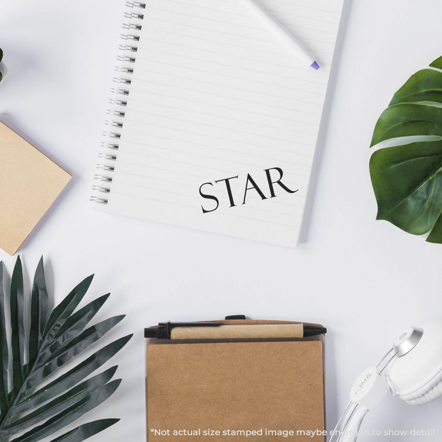 A star rubber stamp impression on a white notebook page, surrounded by office supplies and greenery on a white desk.