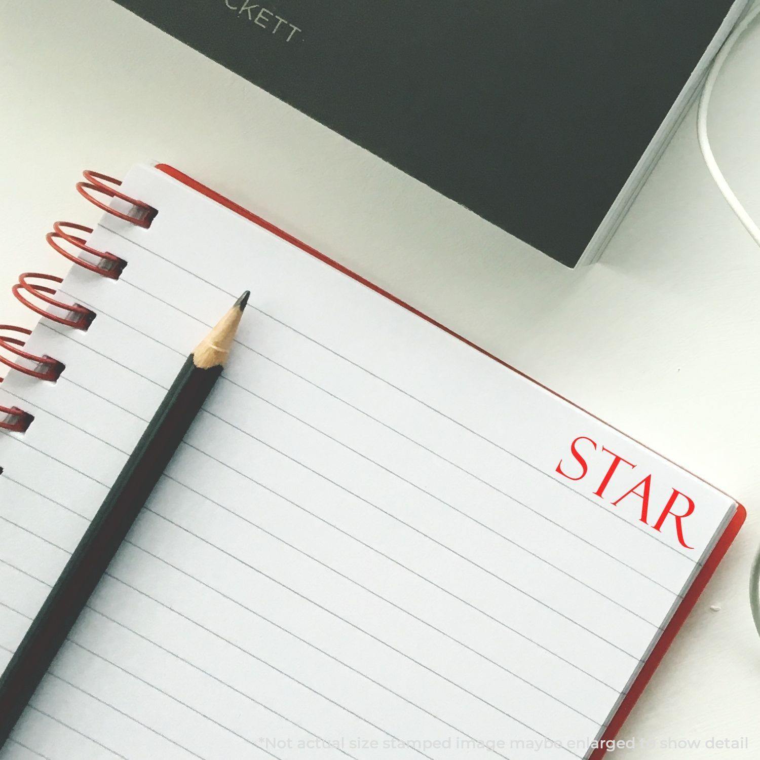 A Large Self Inking Star Stamp is used on the top right corner of a lined notebook page, with a pencil placed diagonally across the page.