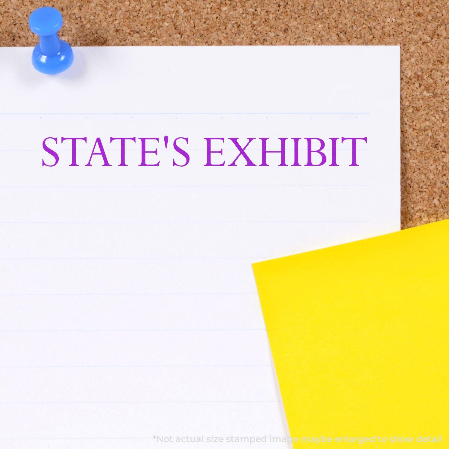 A Large Self Inking State's Exhibit Stamp imprint in purple ink on white paper pinned to a corkboard, with a yellow paper beside it.