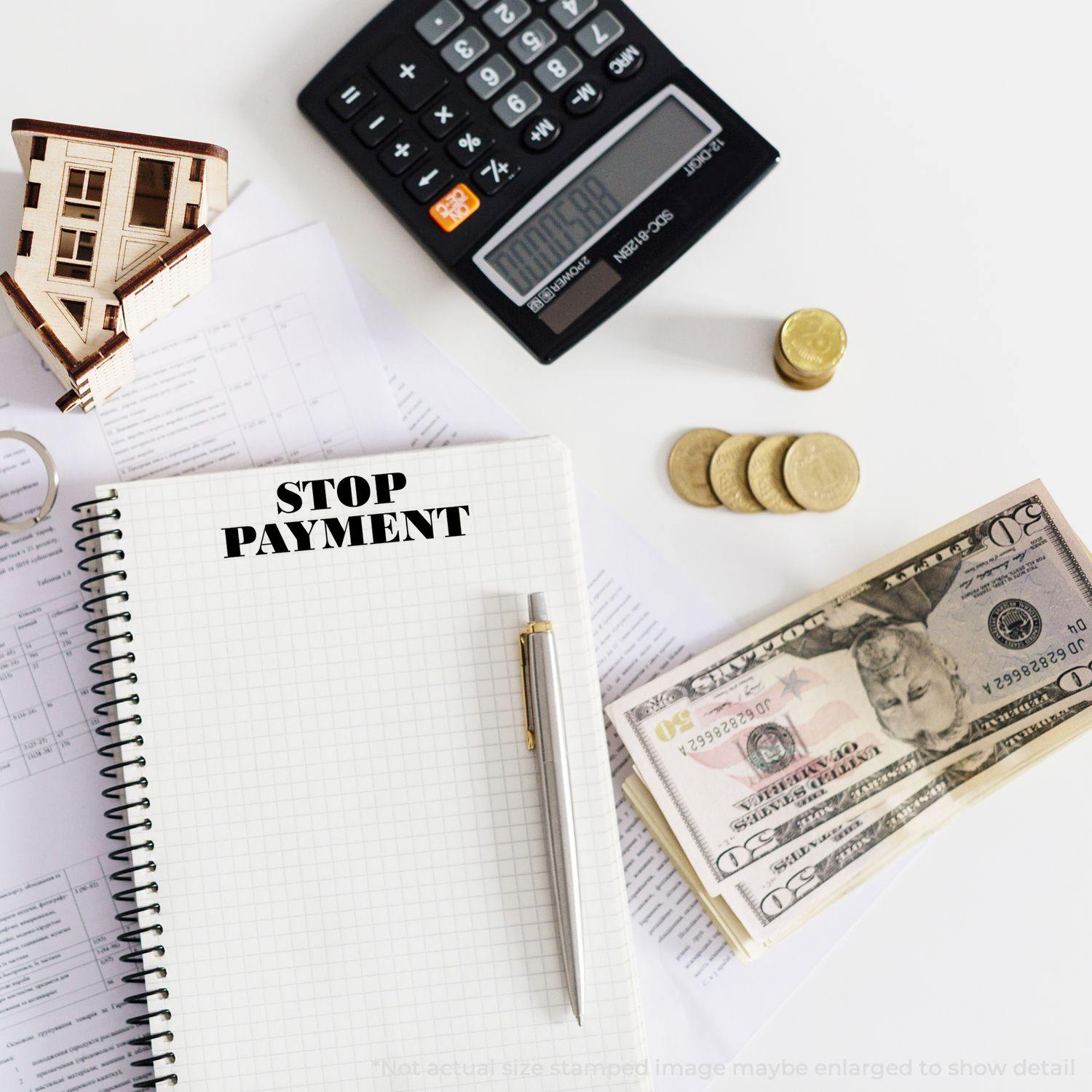 Notebook stamped with STOP PAYMENT using Self Inking Stop Payment Stamp, surrounded by a calculator, coins, and dollar bills on a desk.