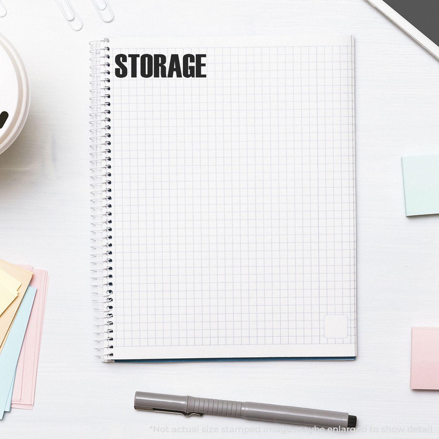 Large Pre-Inked Storage Stamp used on a spiral notebook with grid paper, surrounded by sticky notes, a pen, and paper clips.