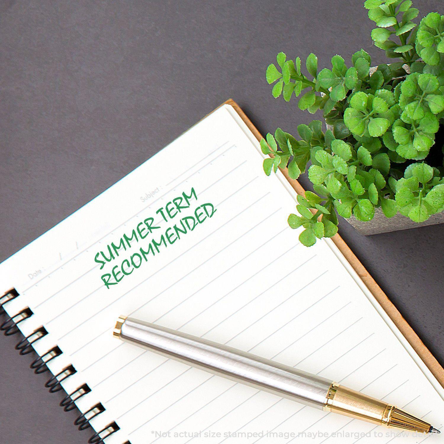 A notebook with SUMMER TERM RECOMMENDED stamped in green ink using the Self Inking Summer Term Recommended Stamp, next to a pen and plant.