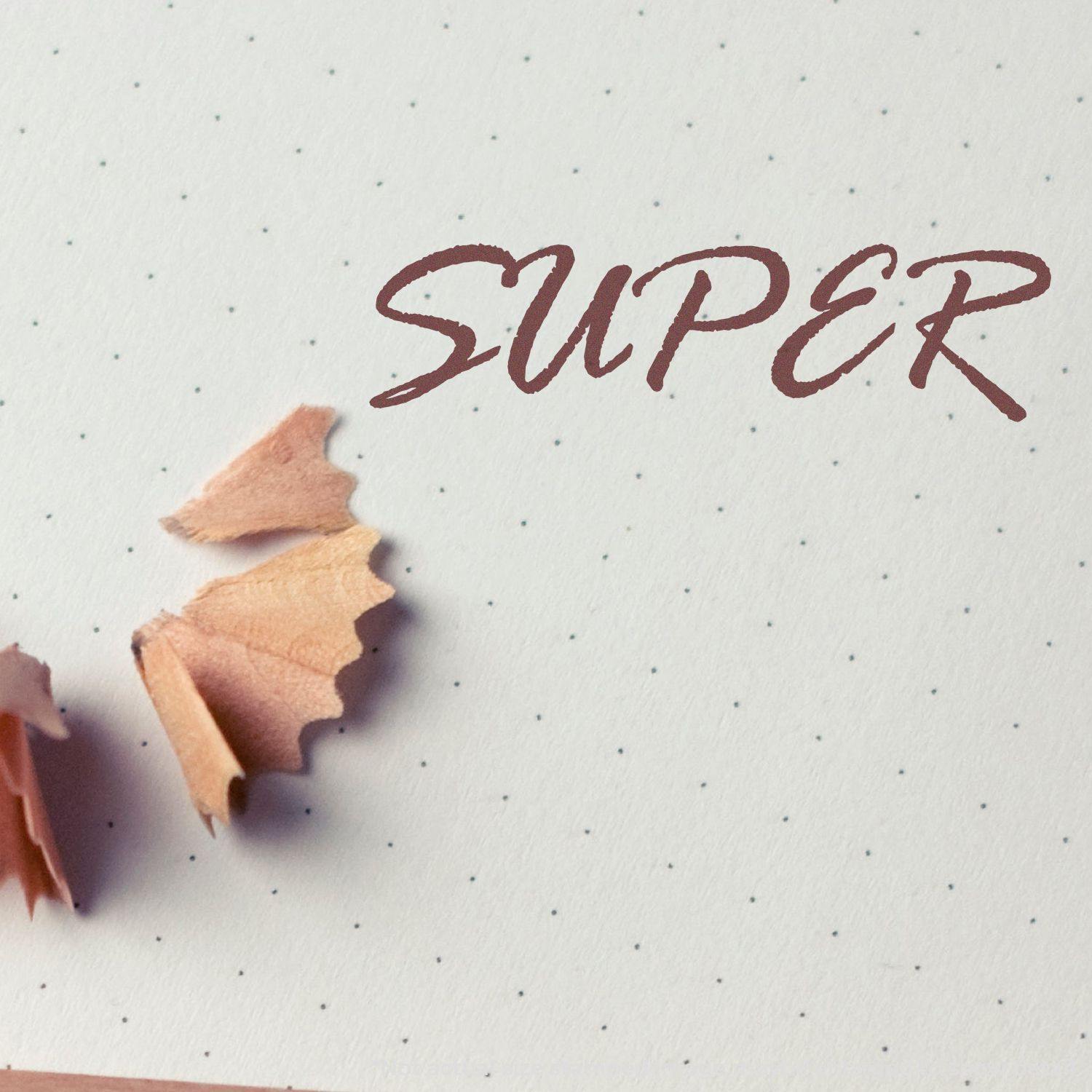 Large Super Rubber Stamp imprinting the word "SUPER" on dotted paper, with pencil shavings nearby.