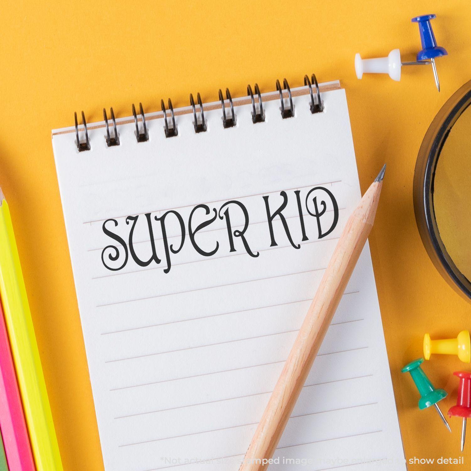 Large Pre-Inked Super Kid Stamp used on a notepad with a pencil, colorful push pins, and a magnifying glass on a yellow background.