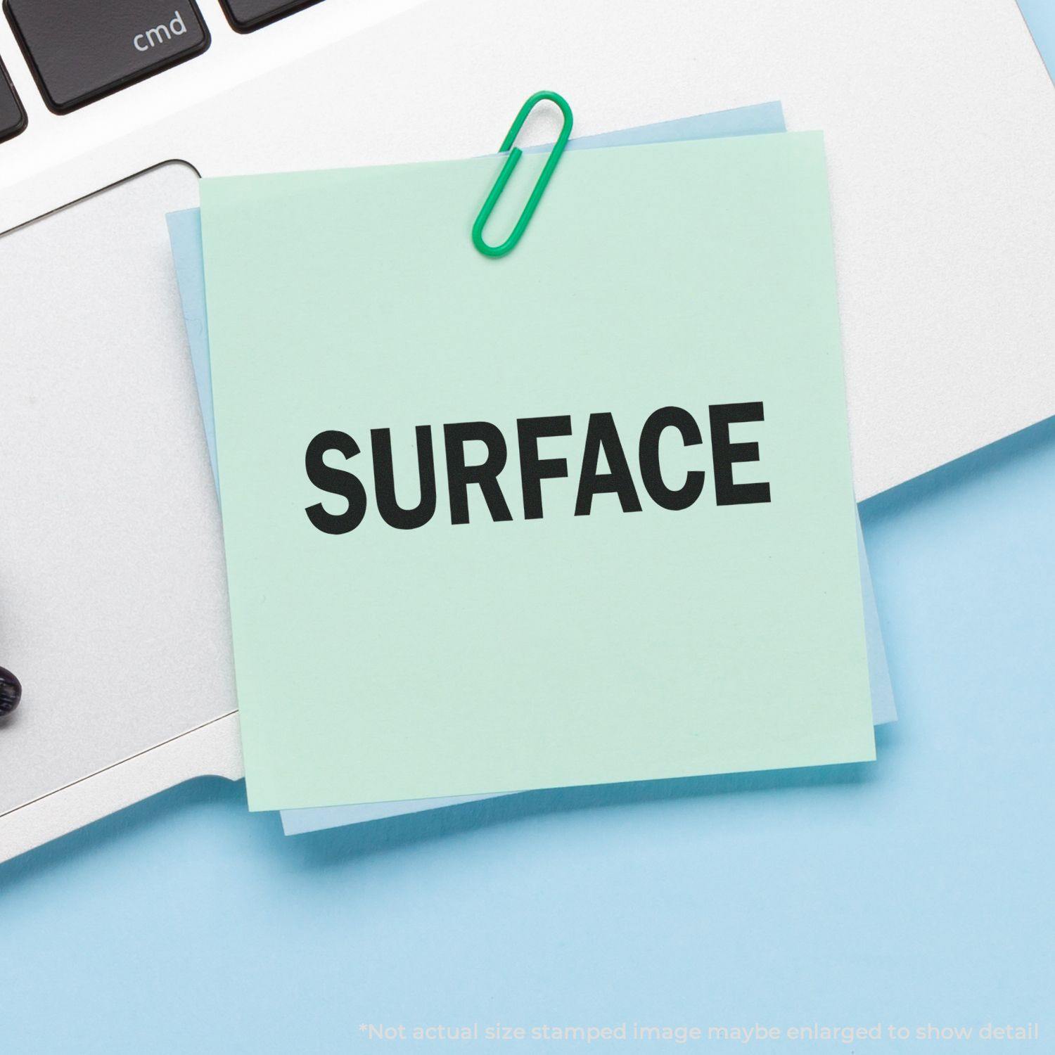 Large Self Inking Surface Stamp imprint on a green sticky note, clipped to a laptop keyboard, showcasing the clear and bold text SURFACE .