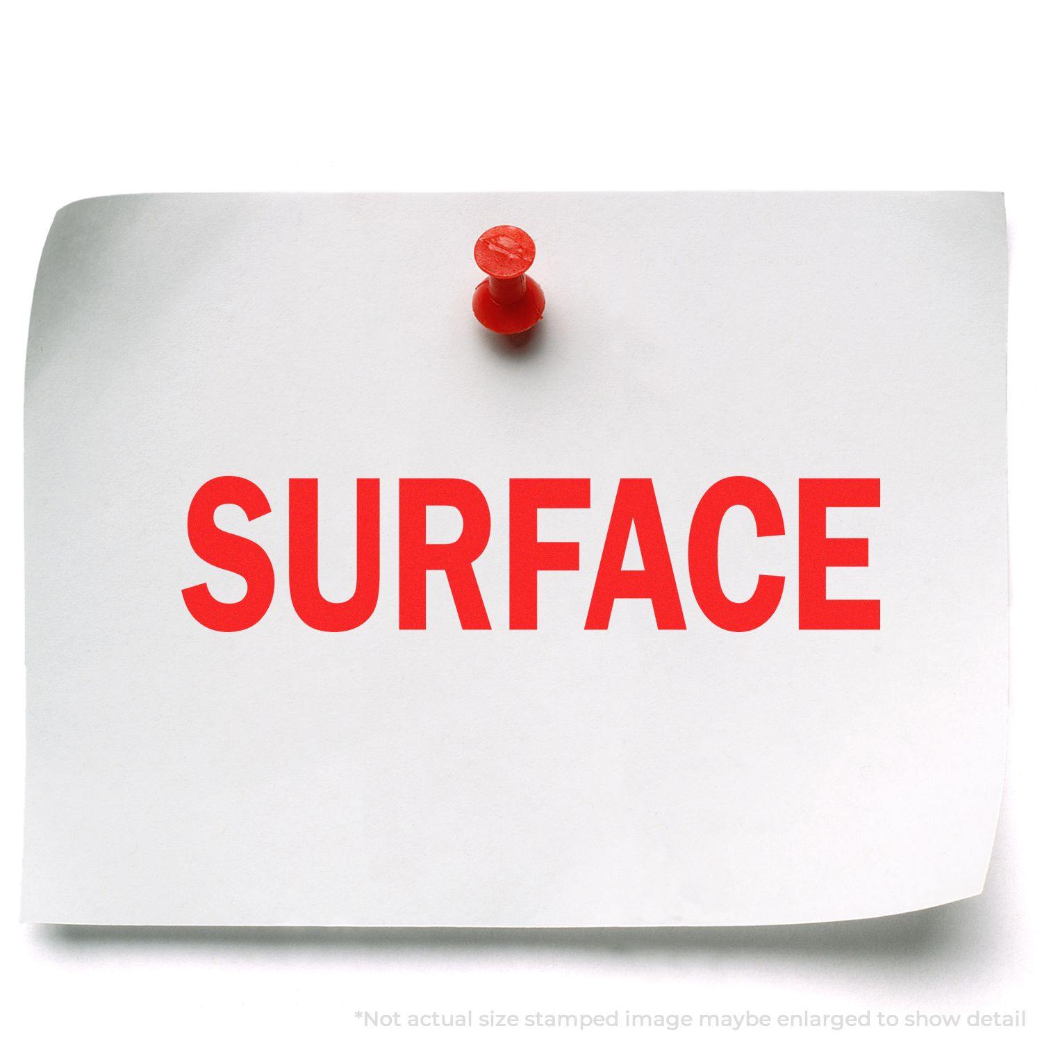 A white paper with the word SURFACE stamped in red using the Large Pre-Inked Surface Stamp, pinned to a white background with a red pushpin.