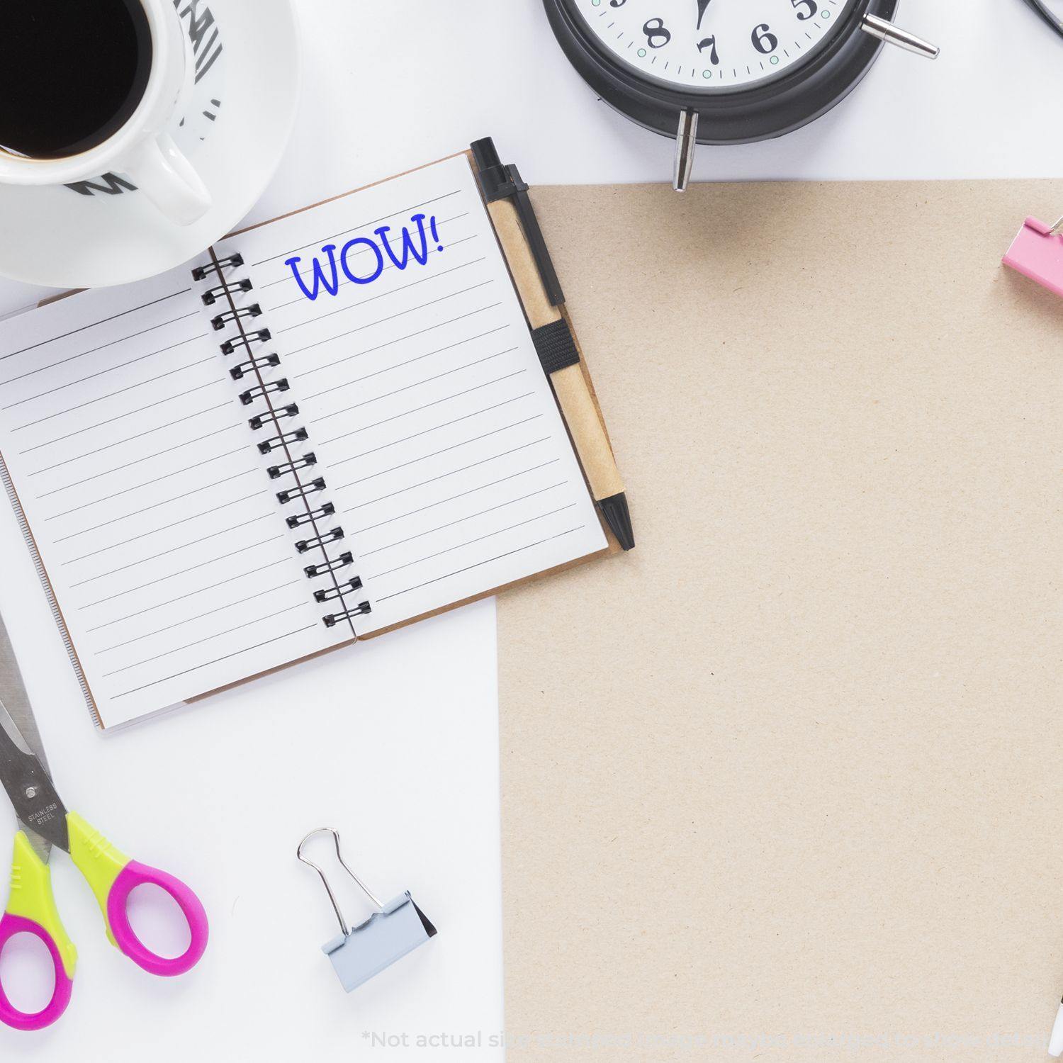 Self Inking WOW Stamp used on a notebook, surrounded by a clock, scissors, binder clip, and coffee cup on a white desk.