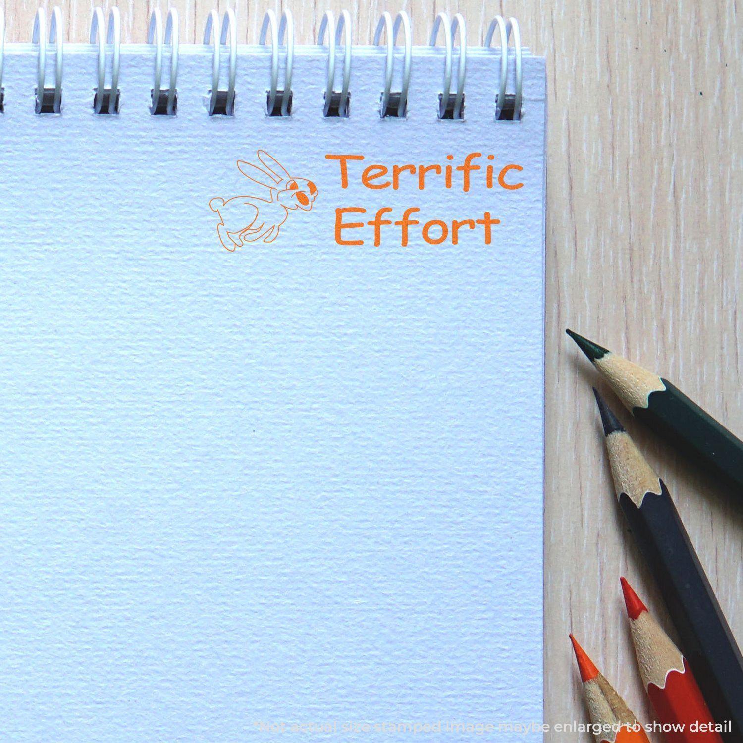 A stock office rubber stamp with a stamped image showing how the text "Terrific Effort" in a large font with an image of a hopping rabbit on the left side is displayed after stamping.