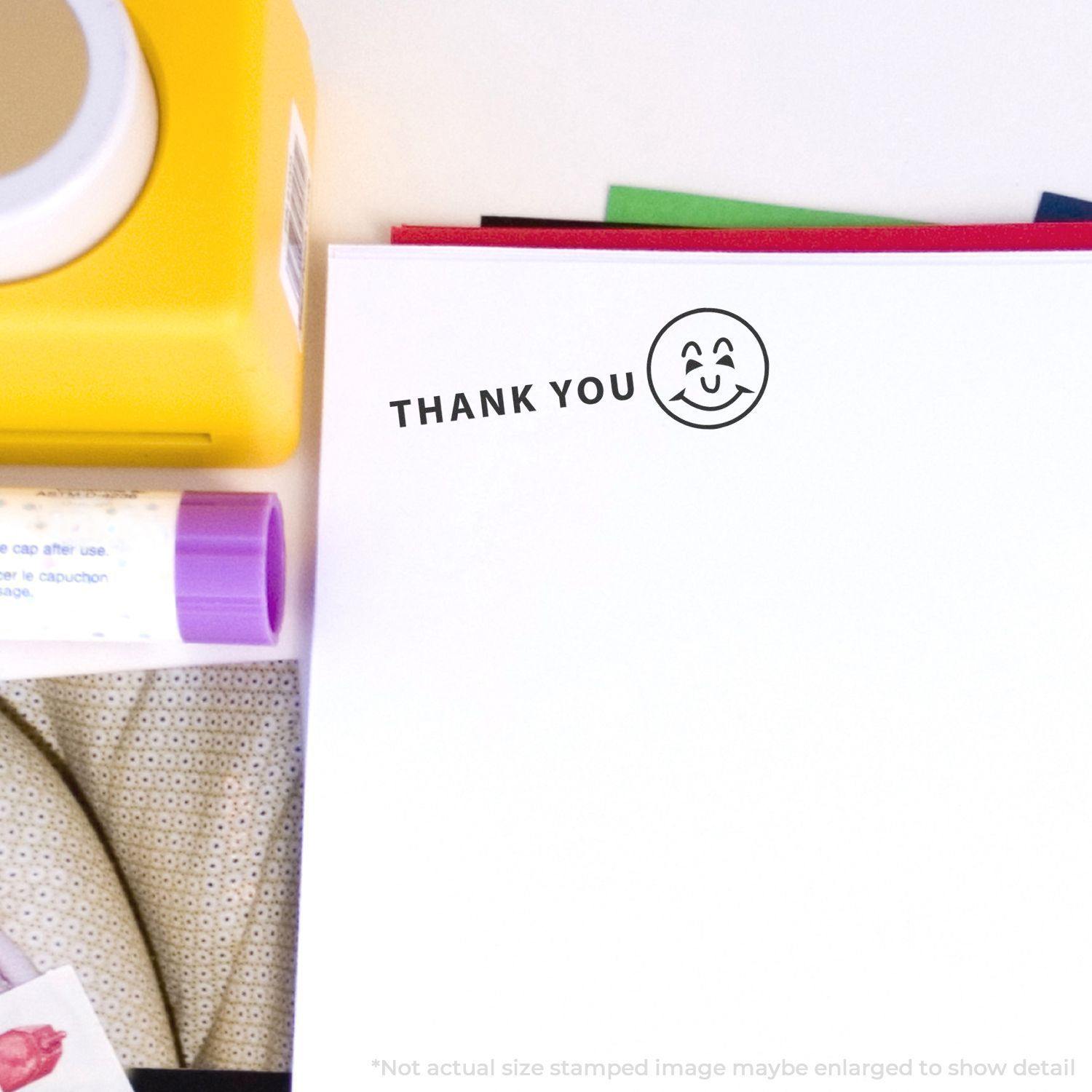 A self-inking stamp with a stamped image showing how the text "THANK YOU" in a large font with an image of a Smiley face on the right side is displayed after stamping.