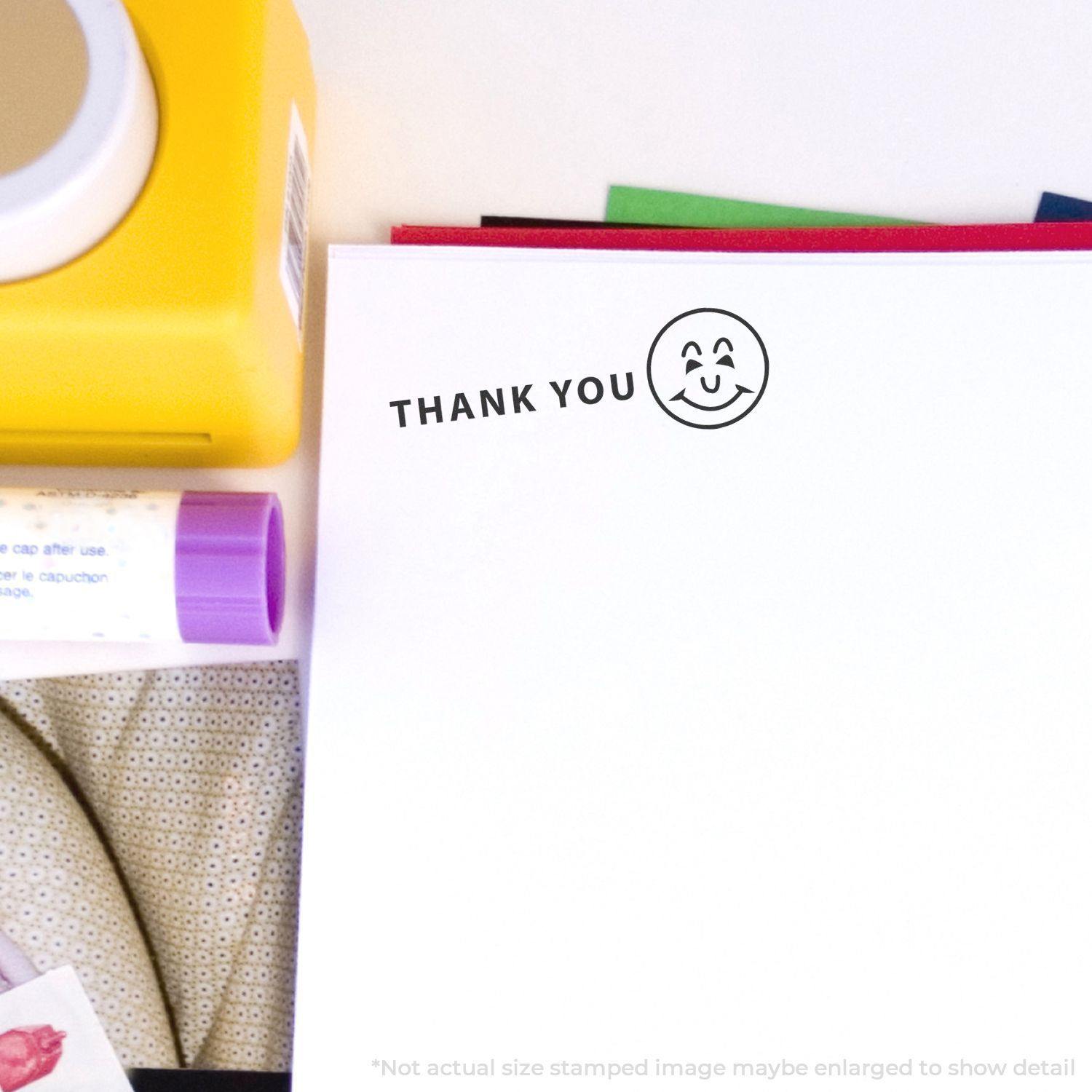 Thank You with Smiley Rubber Stamp on white paper, surrounded by colorful stationery items including a yellow box and purple glue stick.