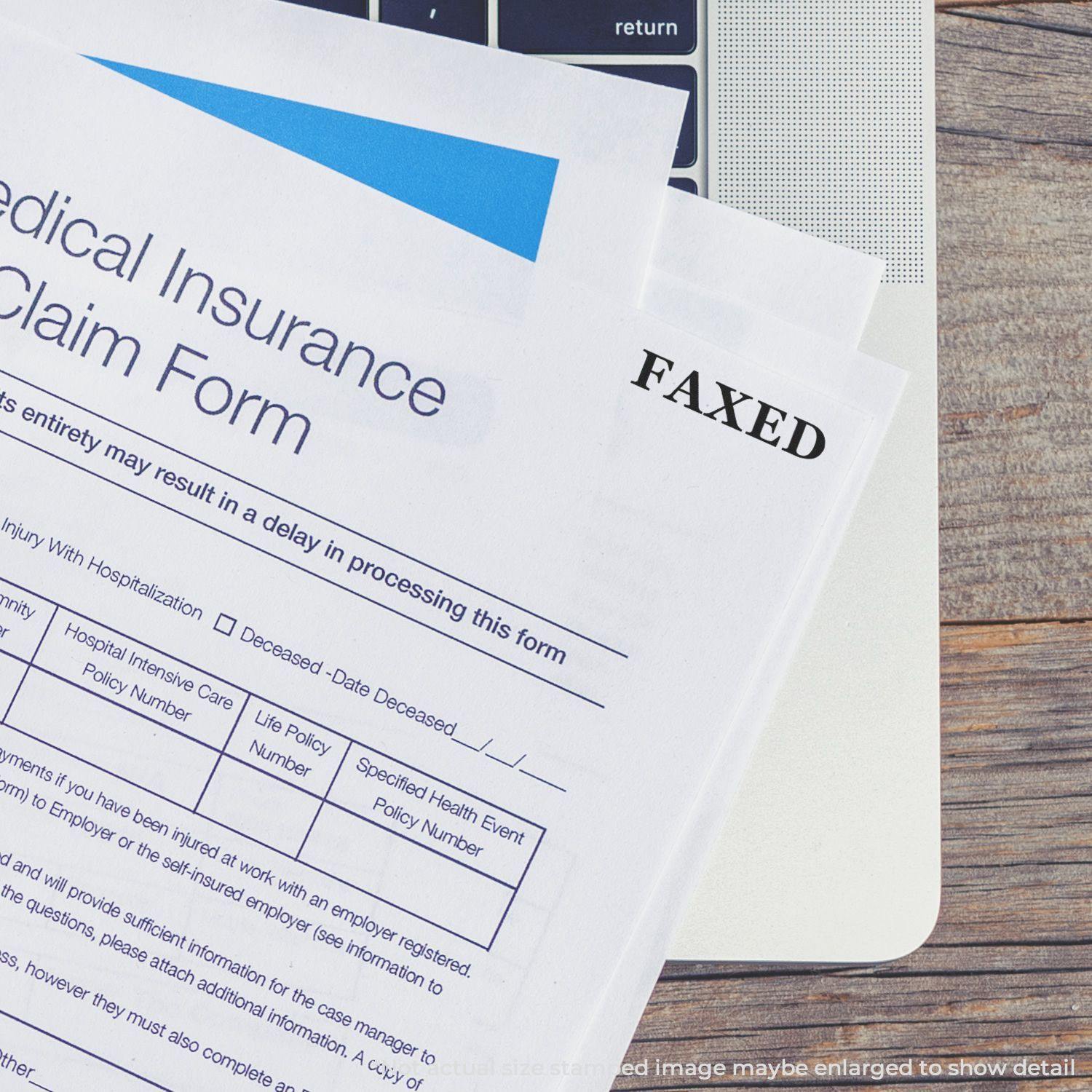 Medical insurance claim form stamped with FAXED using the Large Pre-Inked Times Faxed Stamp, placed on a laptop keyboard.