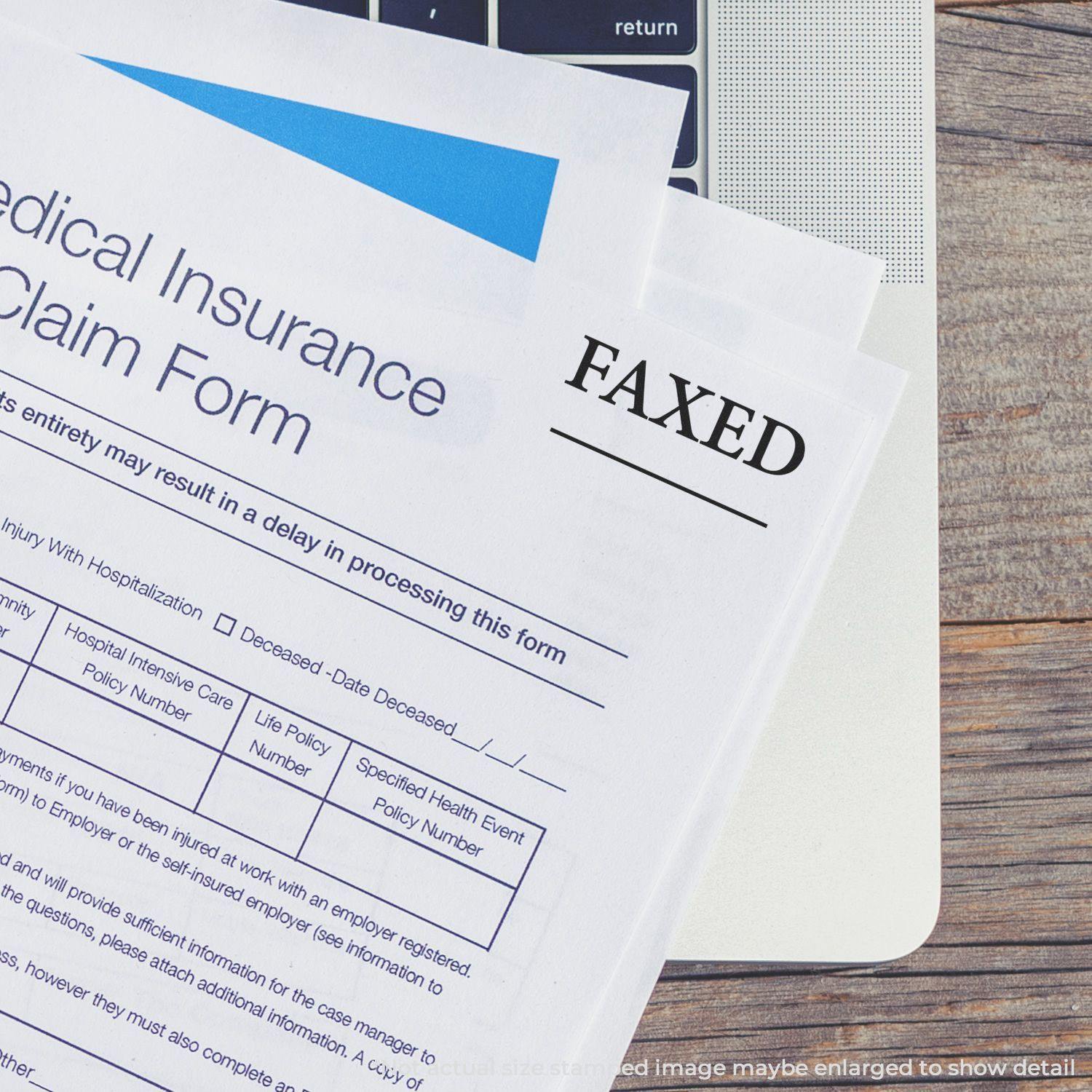 Medical insurance claim form with FAXED stamped in black ink, placed on a laptop keyboard. Large Times Faxed with Line Rubber Stamp.