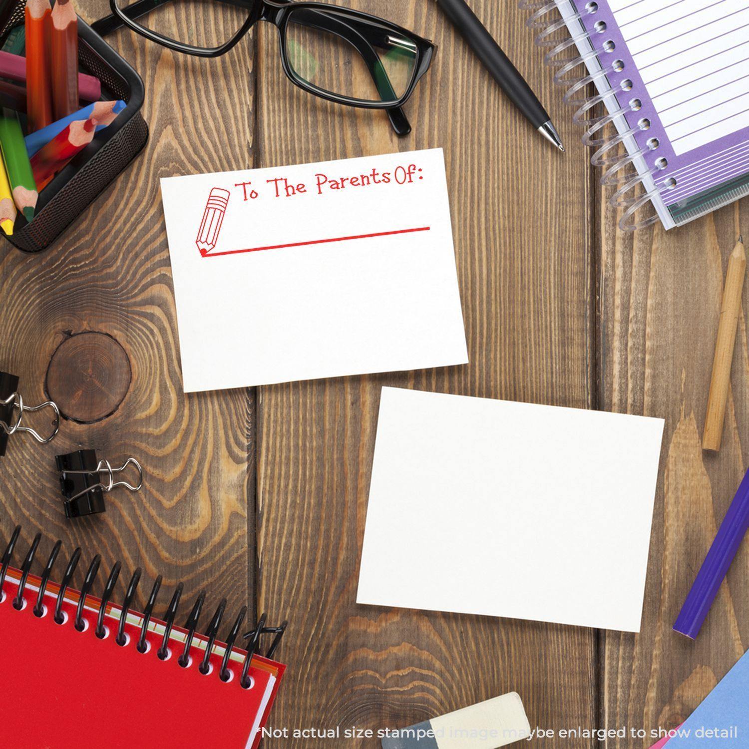 Large Pre-Inked To The Parents Of with Line Stamp in red ink on a white card, surrounded by office supplies on a wooden desk.